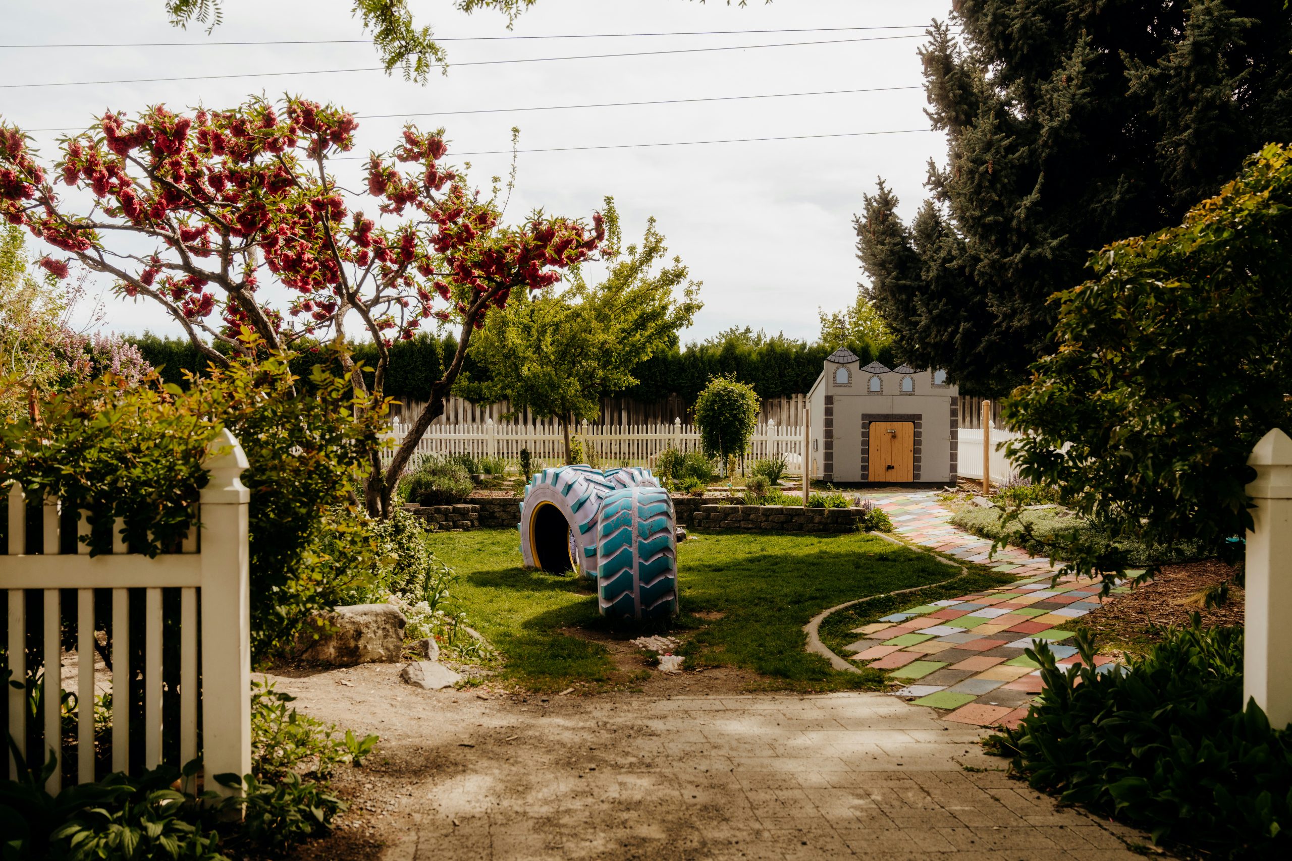 A backyard with a playhouse, tire swing, and garden.