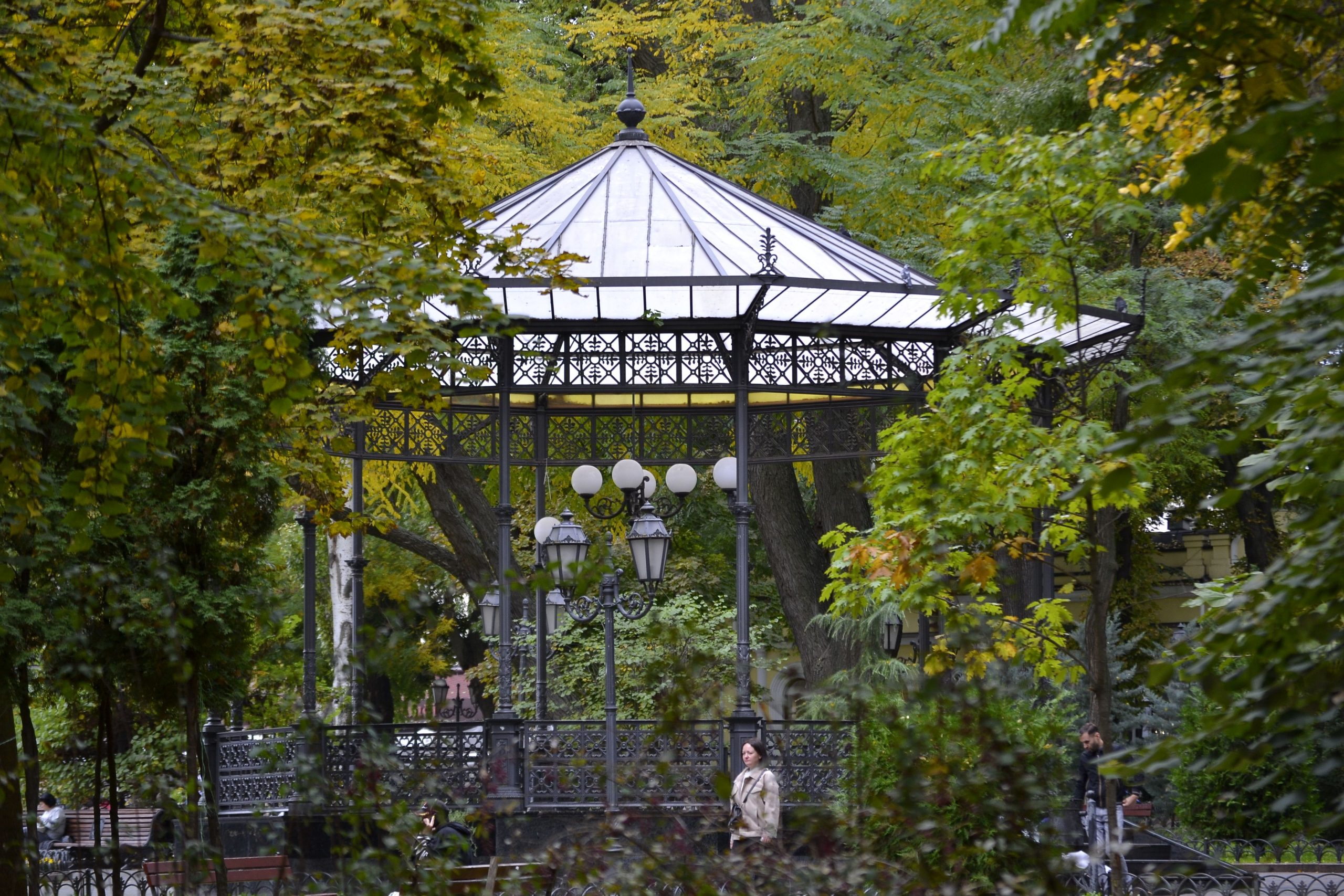 A beautiful metal gazebo surrounded by lush autumn trees in a peaceful park.