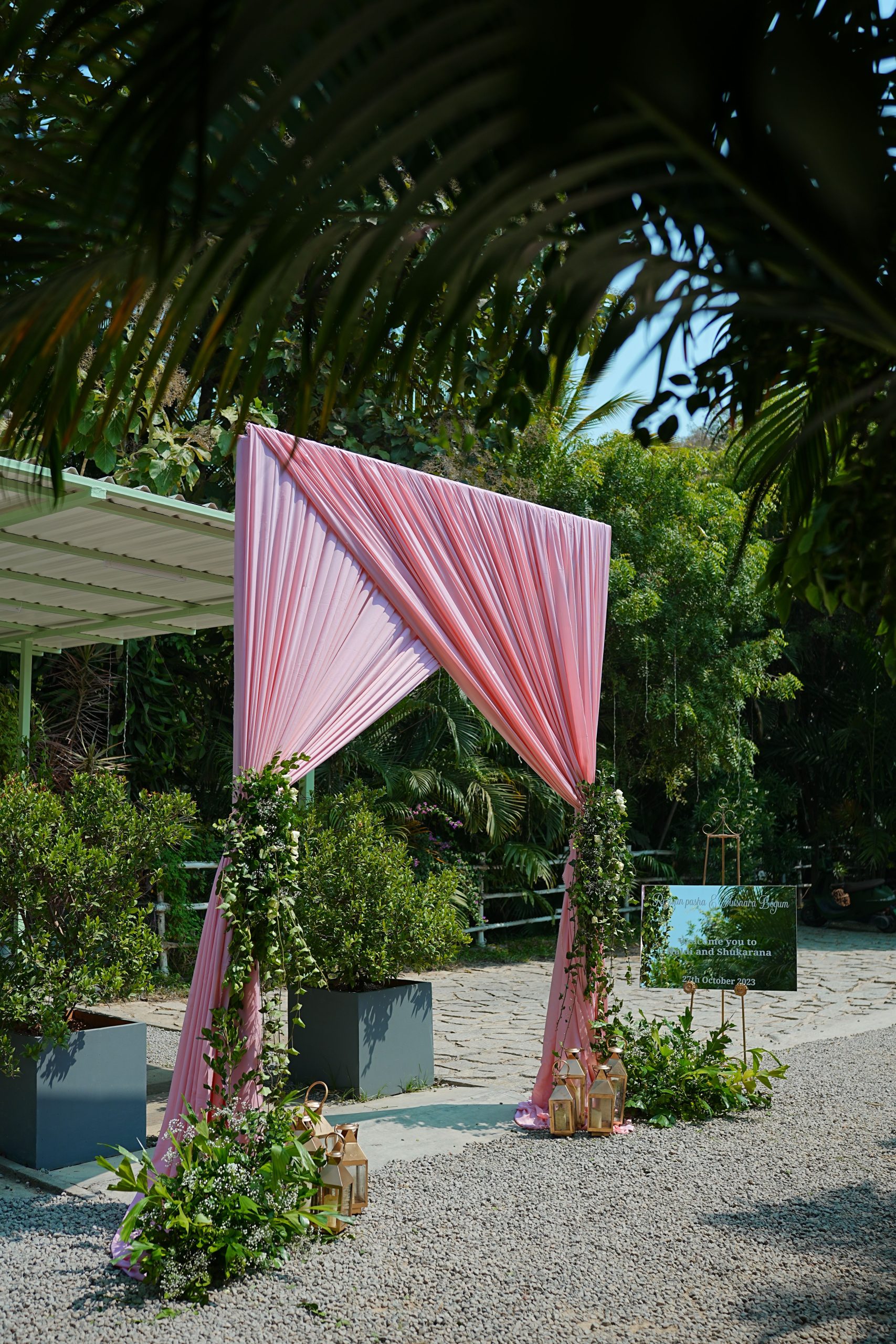 A beautiful outdoor wedding arch decorated with pink fabric and greenery.