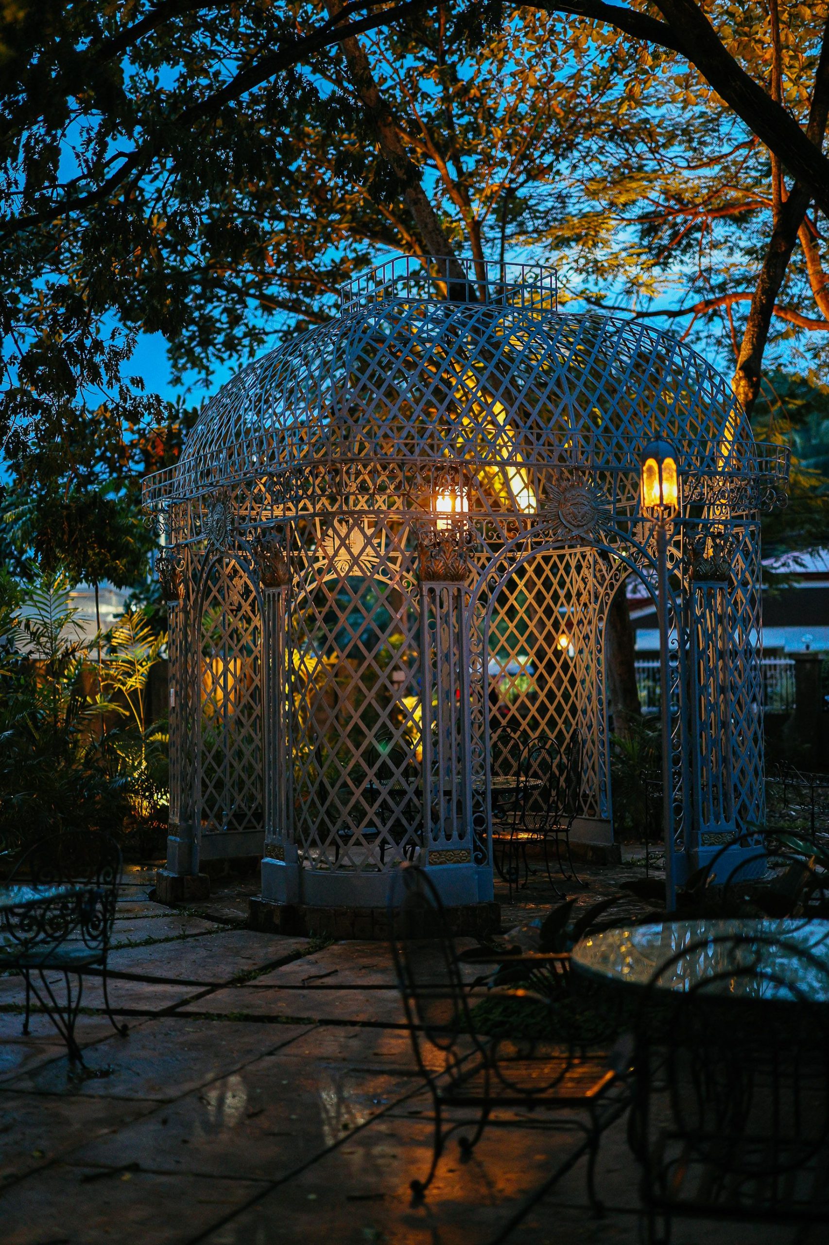 A beautifully ornate garden gazebo illuminated by warm lights during twilight, creating a serene atmosphere.