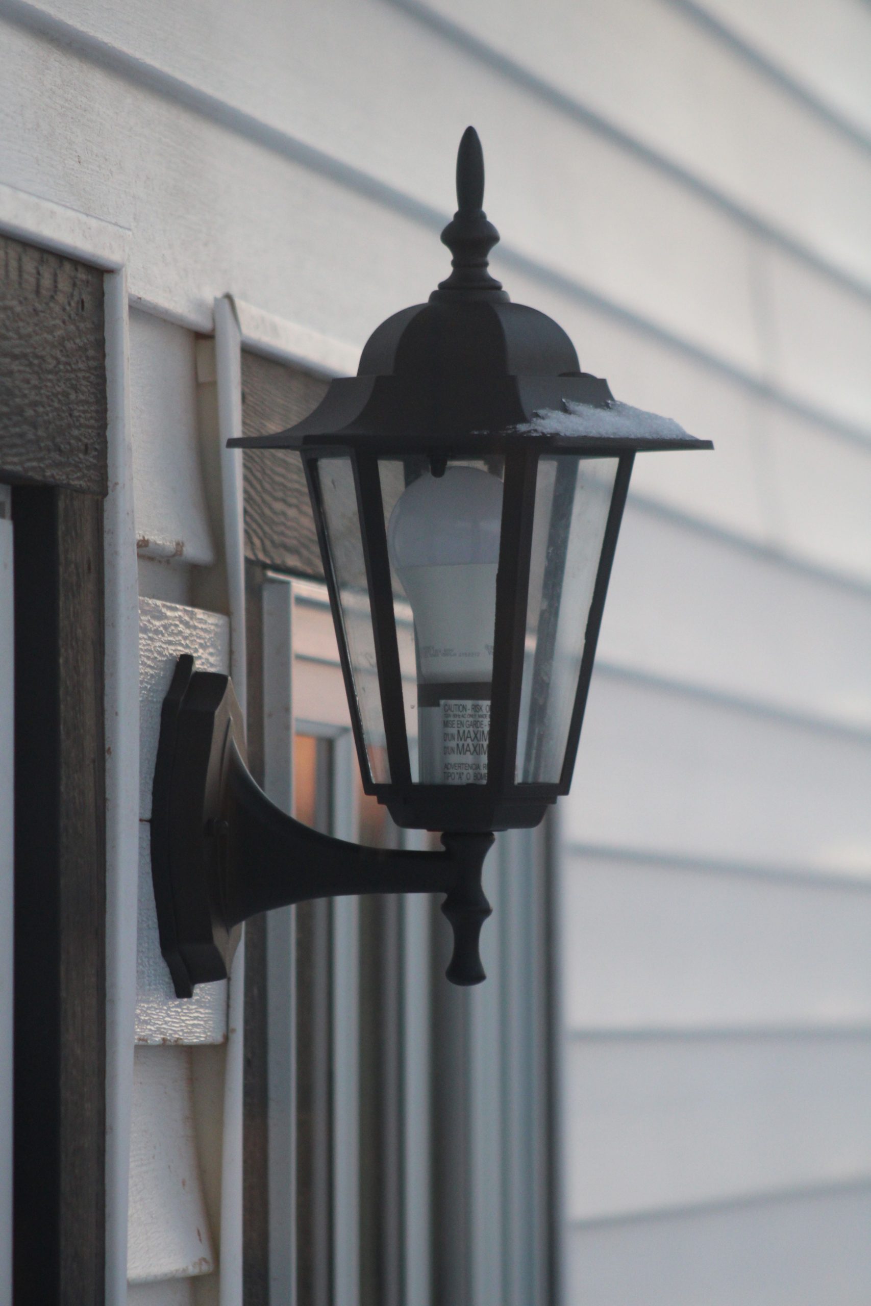 A classic black lantern mounted on a white siding wall, casting a retro vibe.