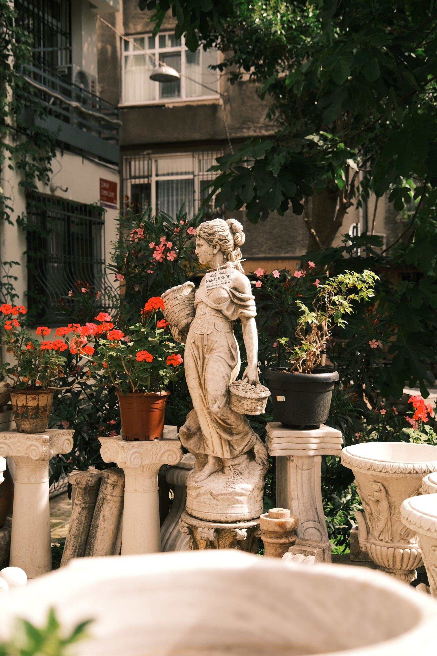 A classical garden statue amidst vibrant potted flowers, creating a serene urban retreat.