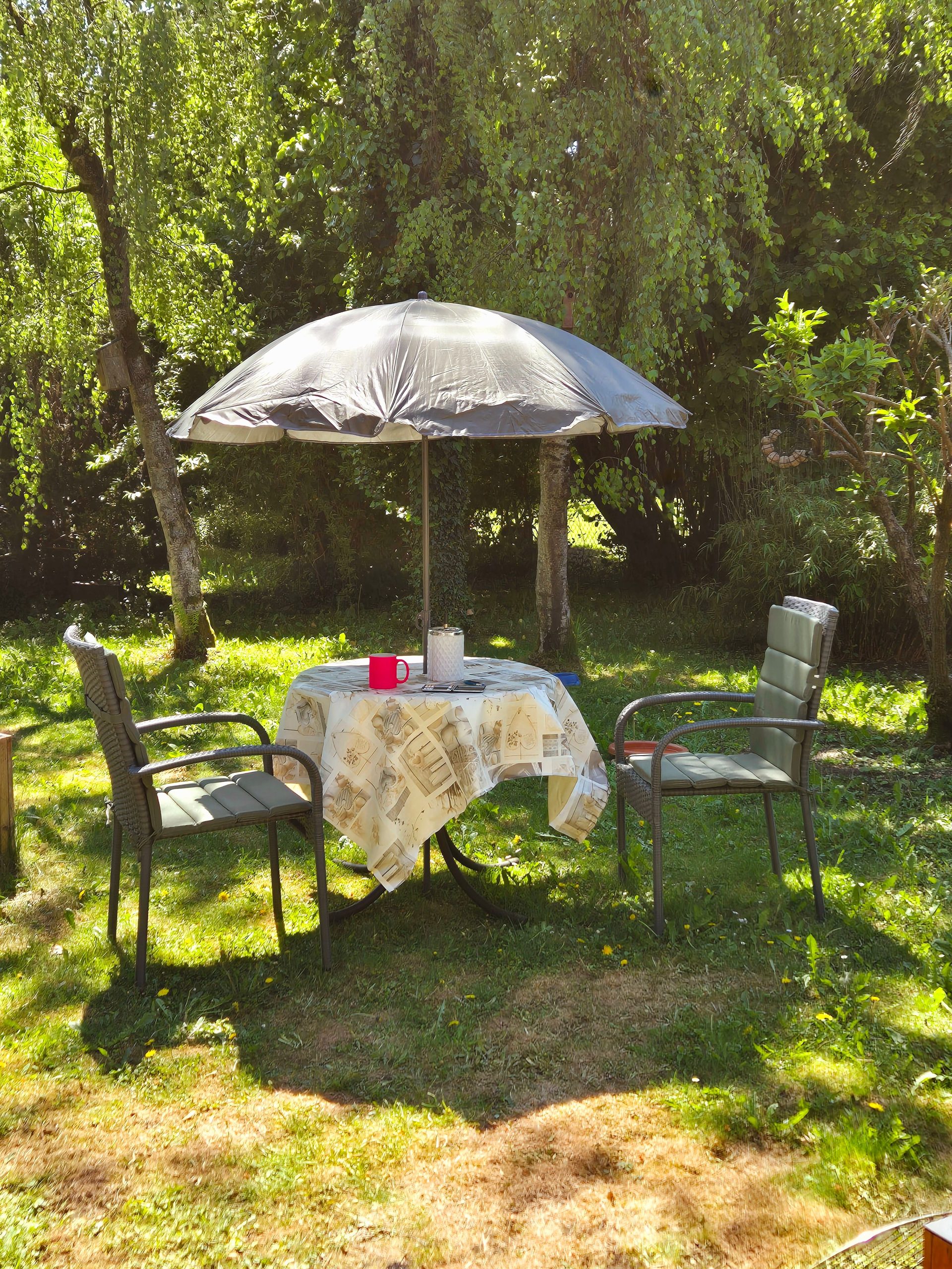 A cozy garden setting with a table and chairs under an umbrella in a sunny park.