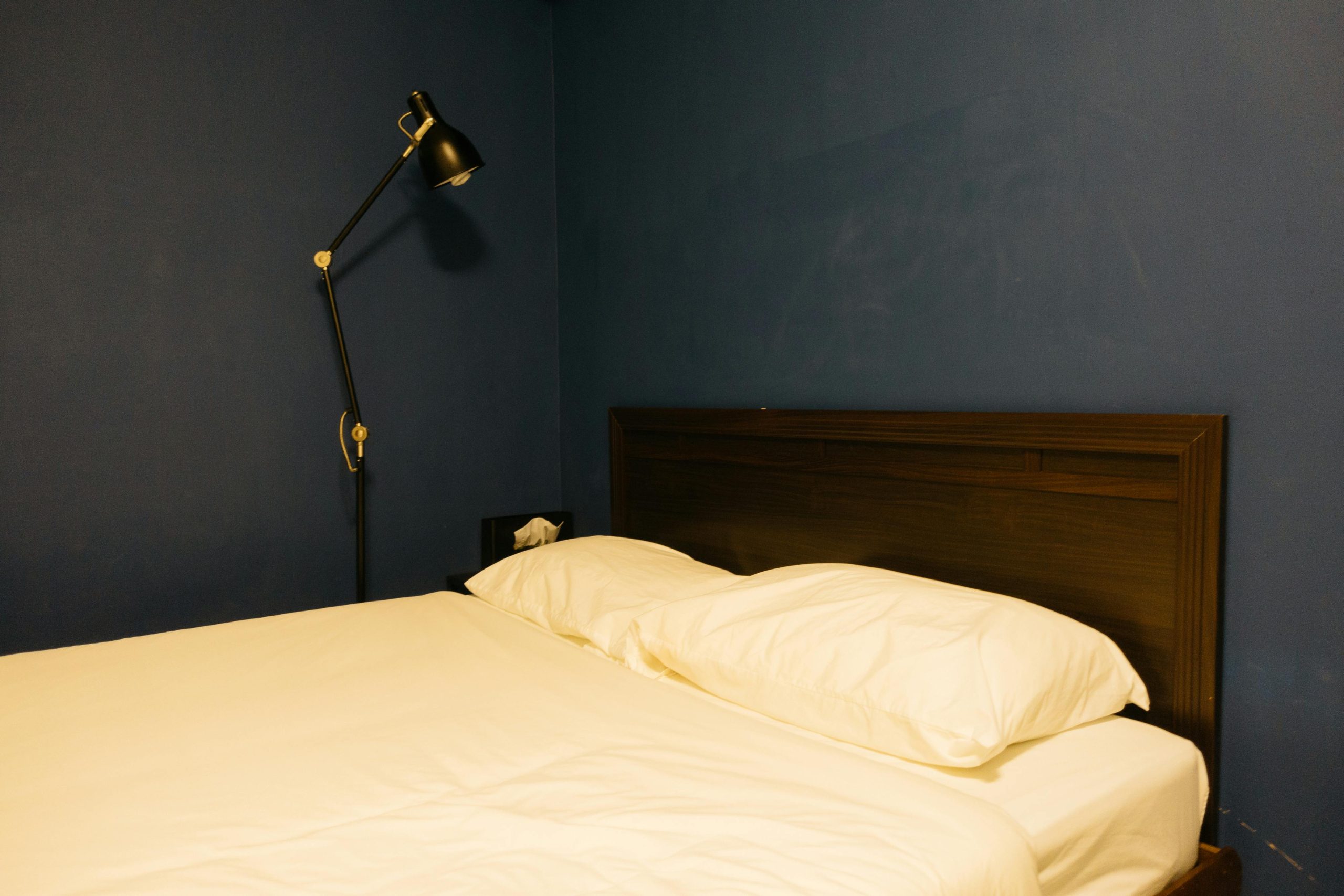 A cozy, minimalist bedroom with a dark blue wall and adjustable lamp.