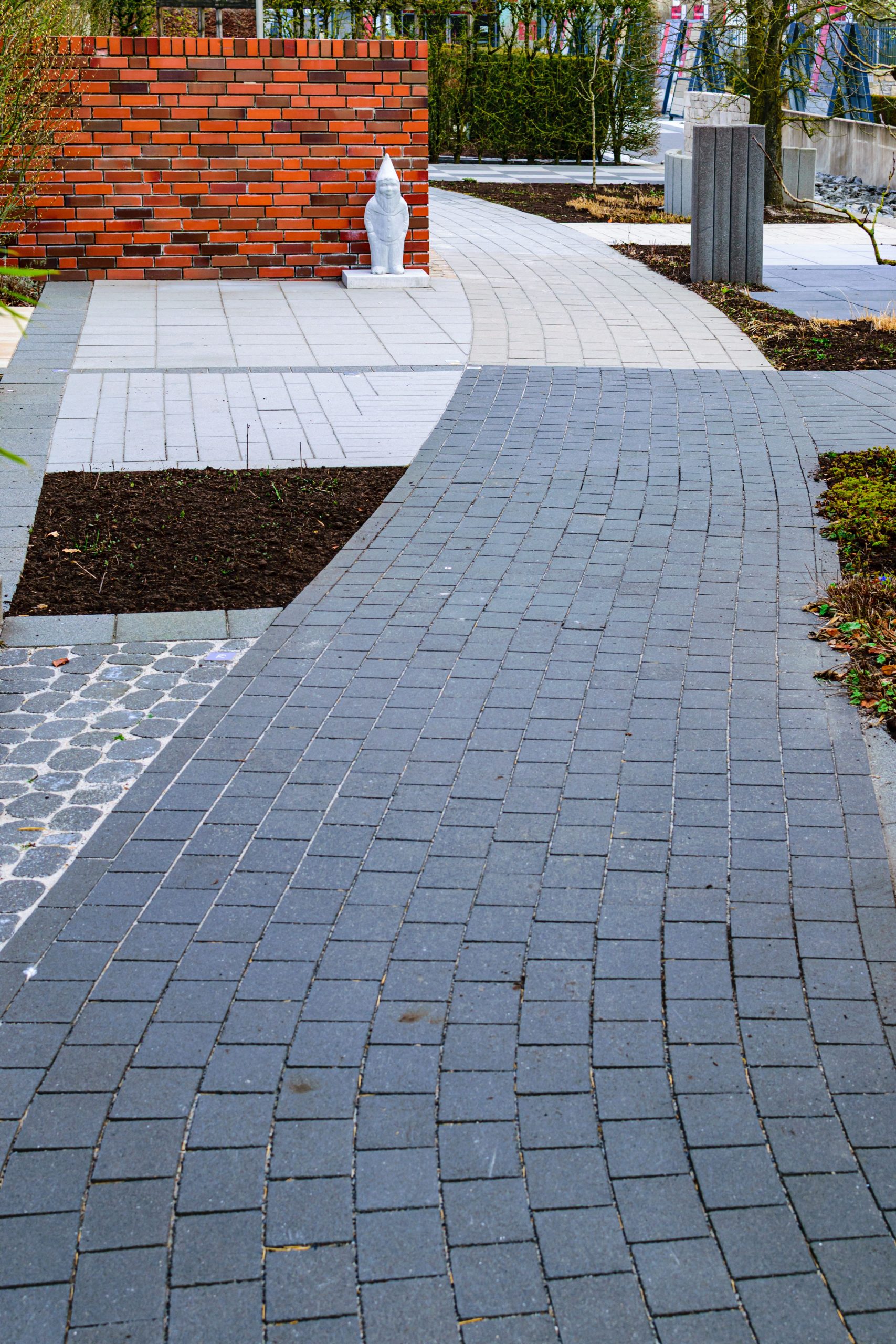 A curved brick pathway in a modern urban garden with red bricks and greenery.