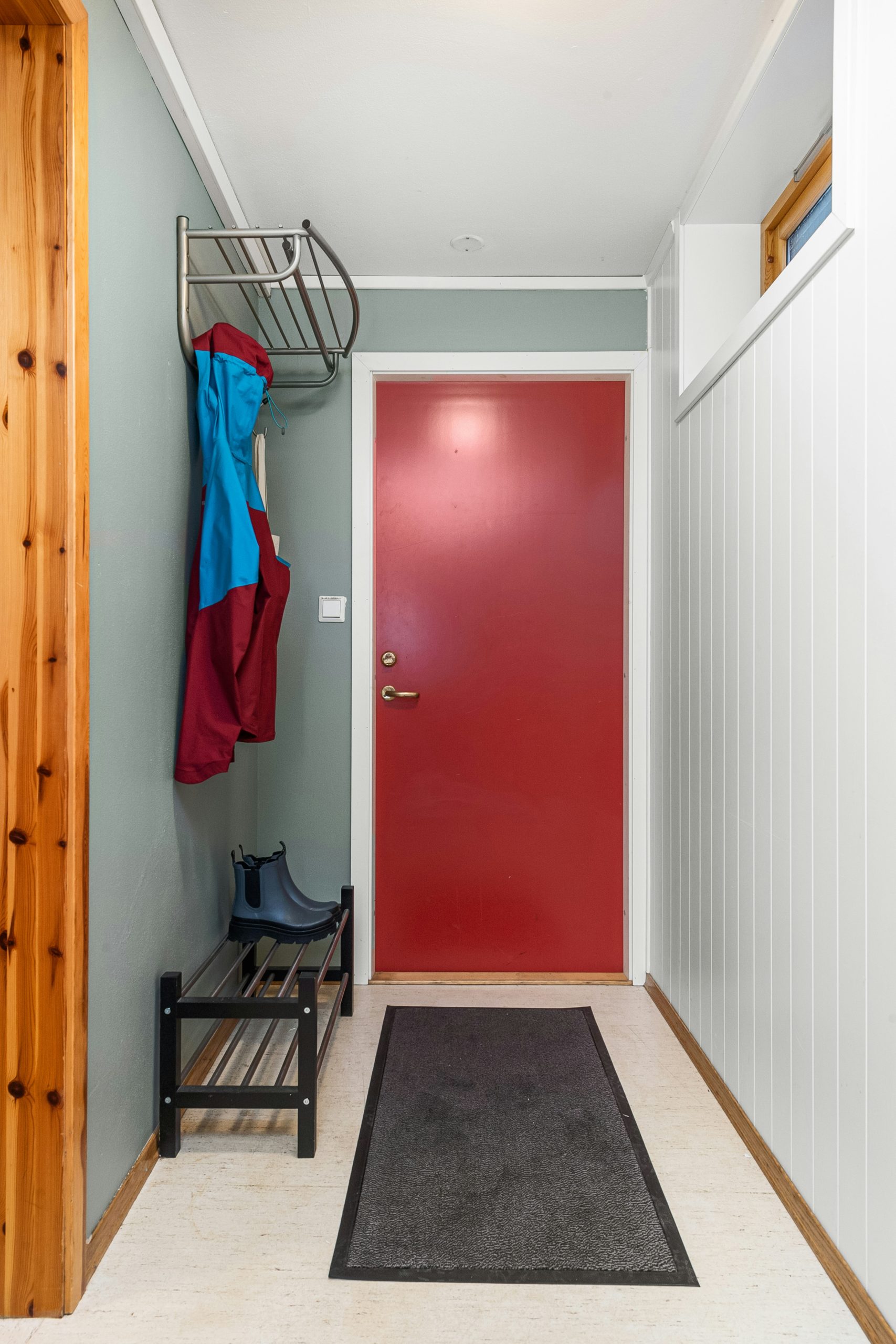 A hallway with a red door and a black rug