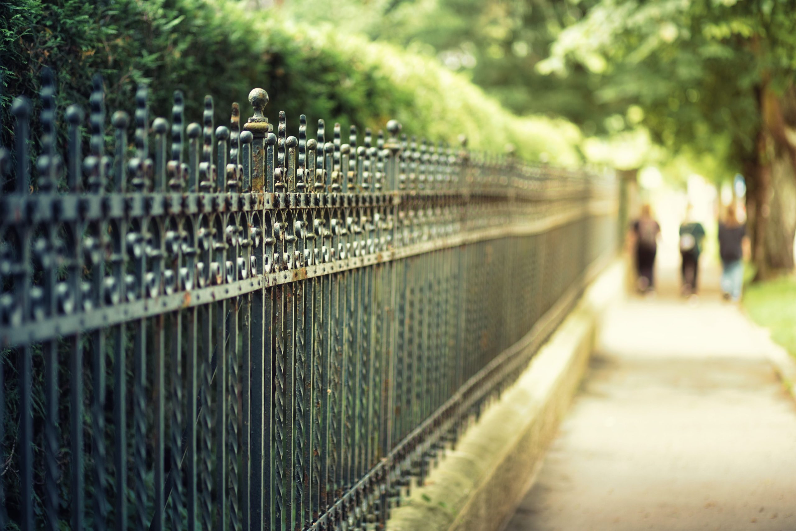 A long iron fence stretches beside a lush, leafy sidewalk in Graz, Austria.