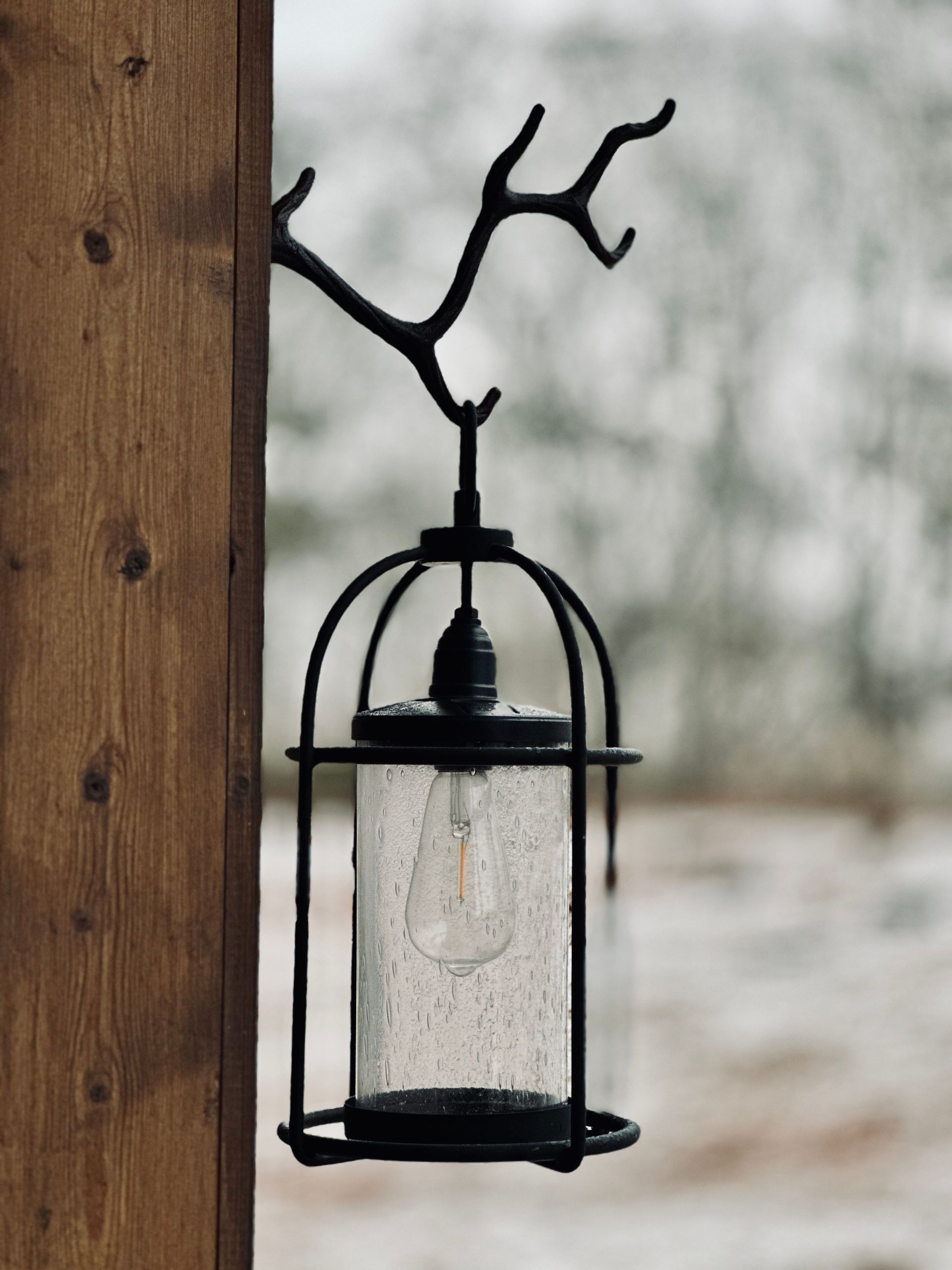 A rustic outdoor lantern hangs from a wooden post with a snowy background.