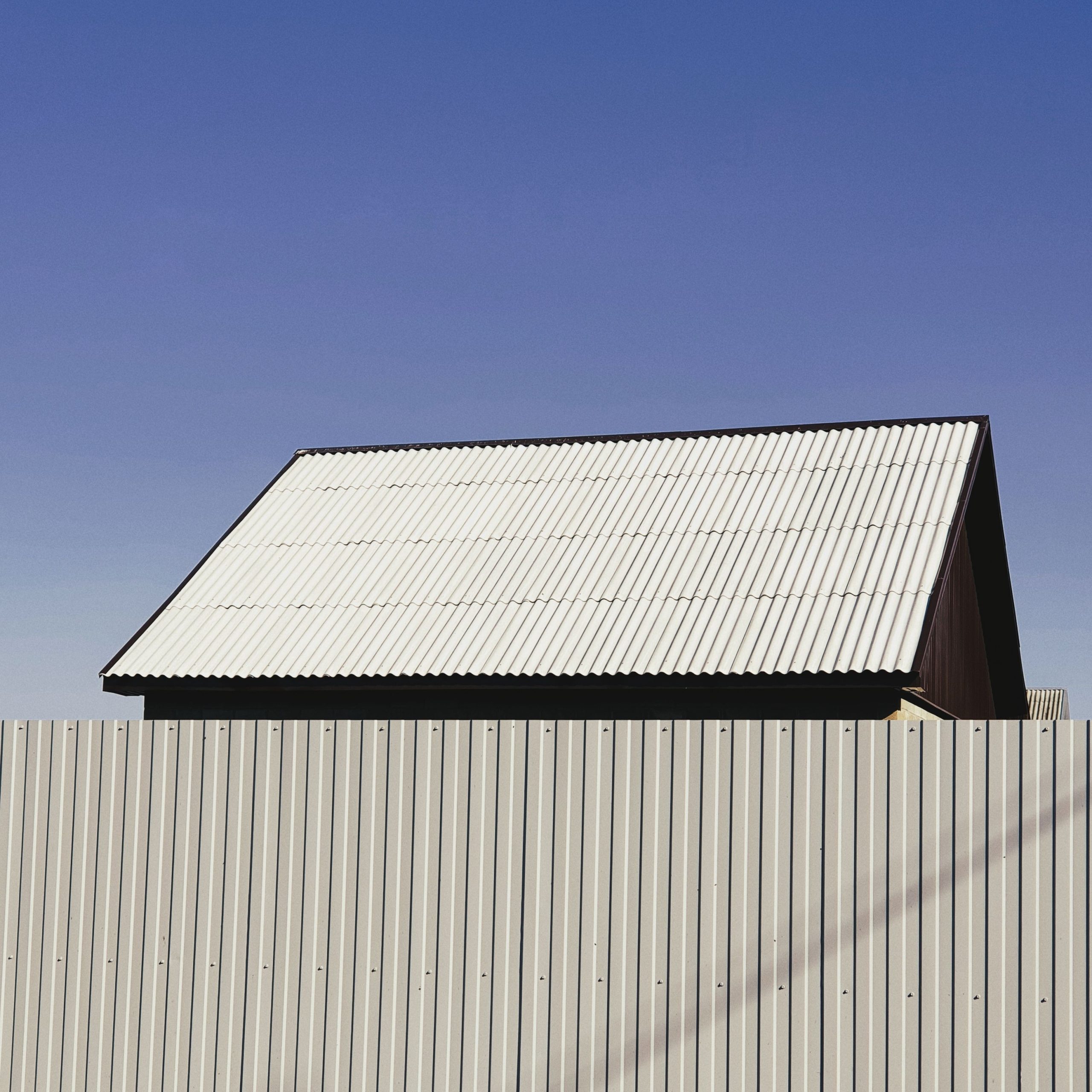 A simple structure with a metal roof and fence under a clear blue sky, showcasing minimalist architecture.