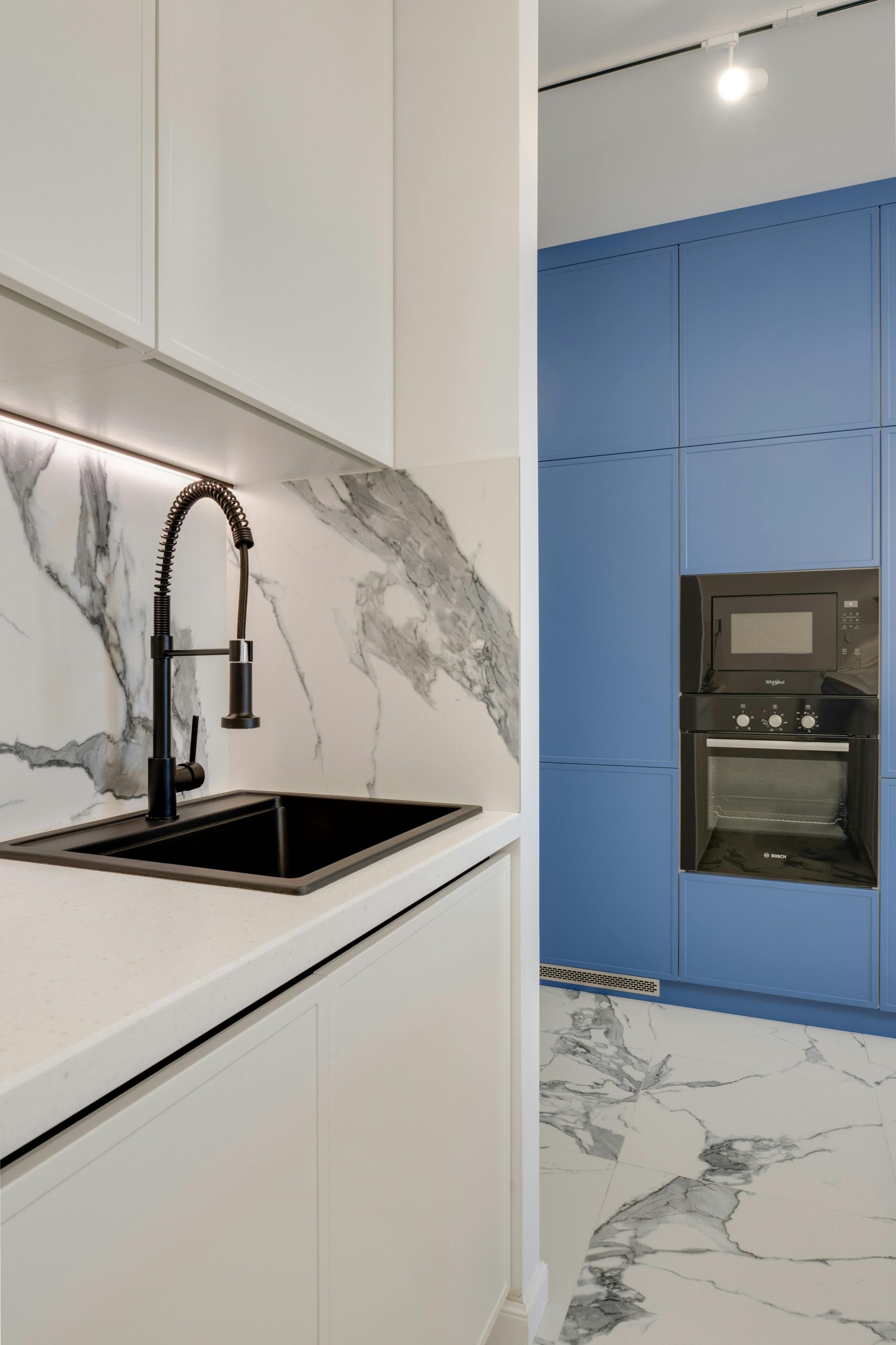 A stylish kitchen with a marble backsplash, black sink, and blue cabinetry.