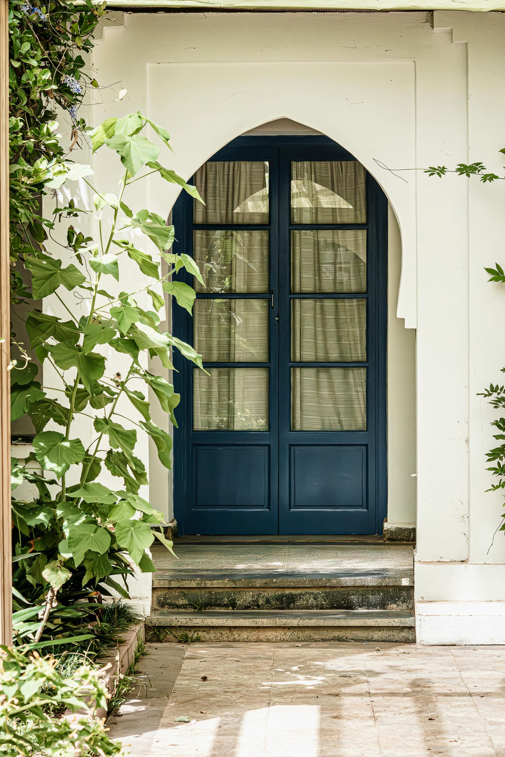 A traditional blue wooden doorway framed by lush greenery and classic architecture, providing a serene entrance.