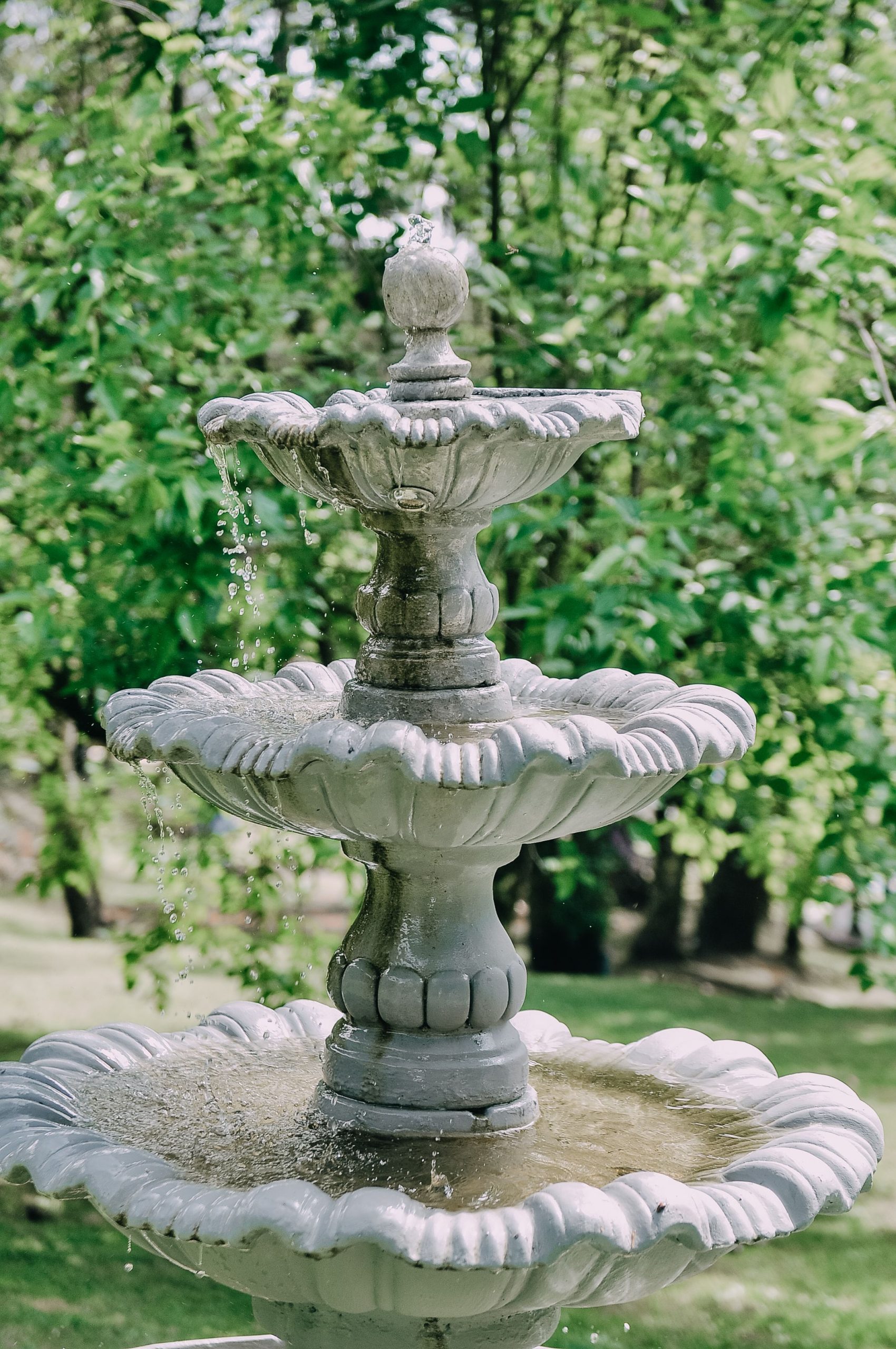 A tranquil three-tier stone fountain with flowing water in a lush green garden, exuding serenity.