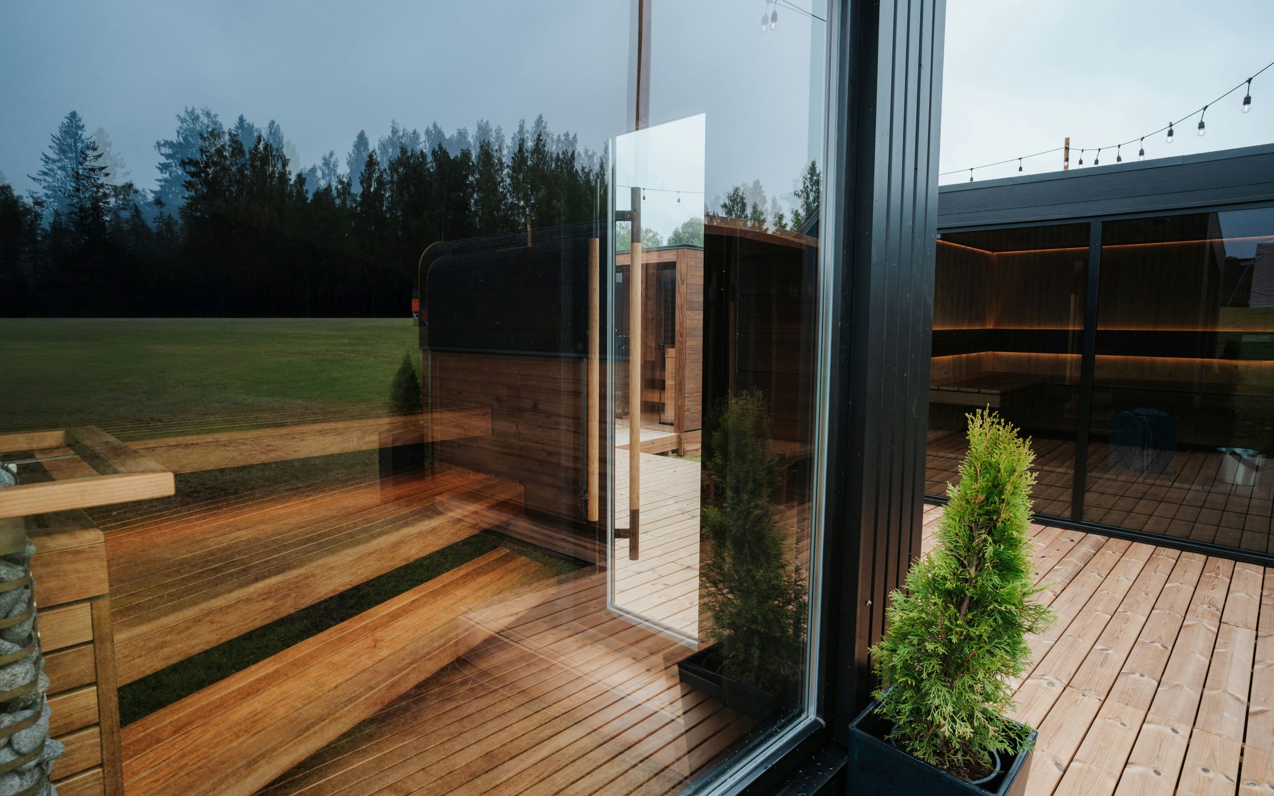 A view of modern sauna cabins with glass walls and warm wooden interiors. Surrounded by greenery and open skies.