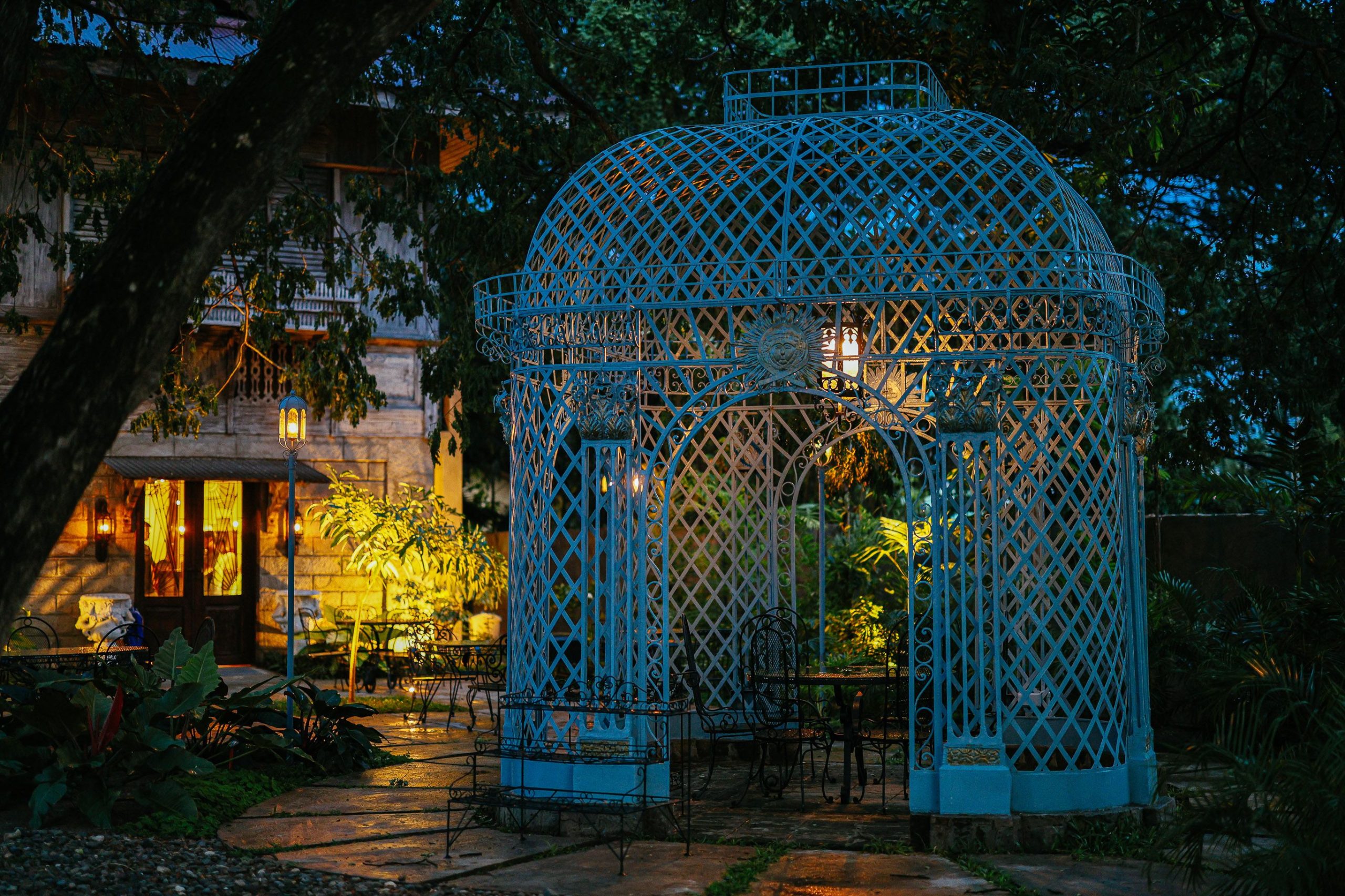 A vintage blue gazebo lit up in a lush garden setting during twilight, offering a serene and picturesque scene.