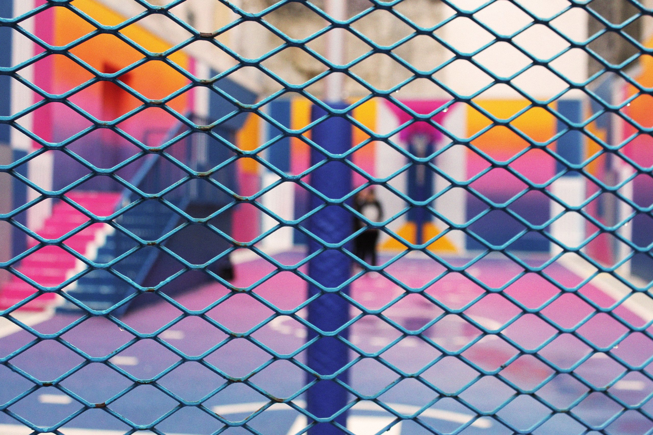 A vivid view of a colorful urban playground seen through a wire fence with blurred background.
