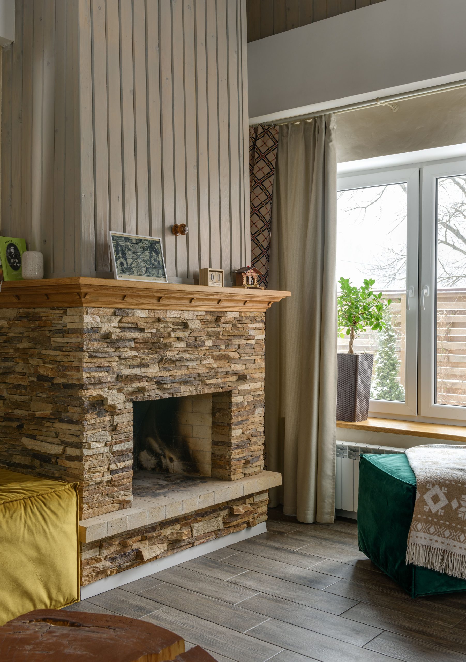 A warm interior featuring a stone fireplace, indoor plant, and natural light through a large window.