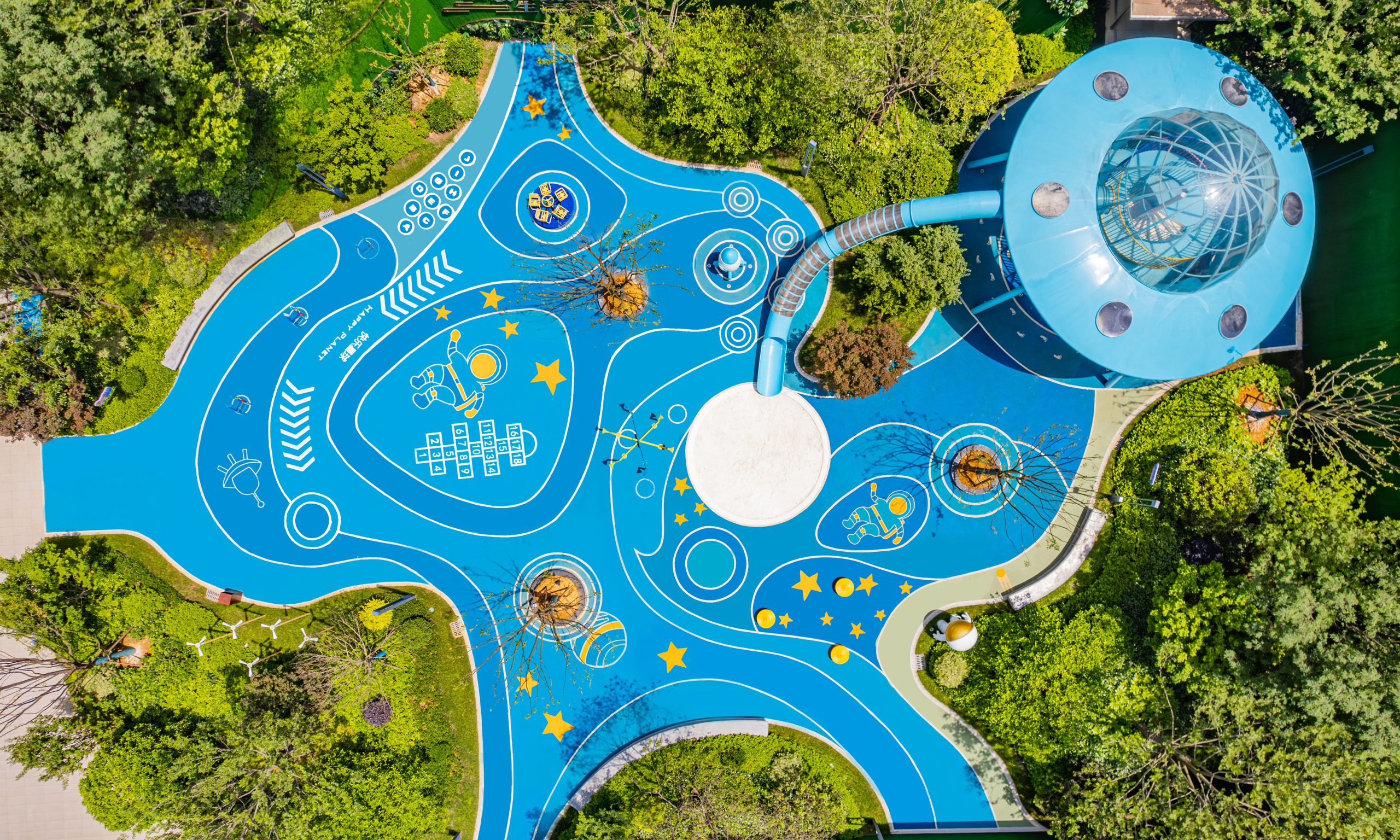 Aerial shot of a vibrant, space-themed playground with blue designs and surrounding greenery.