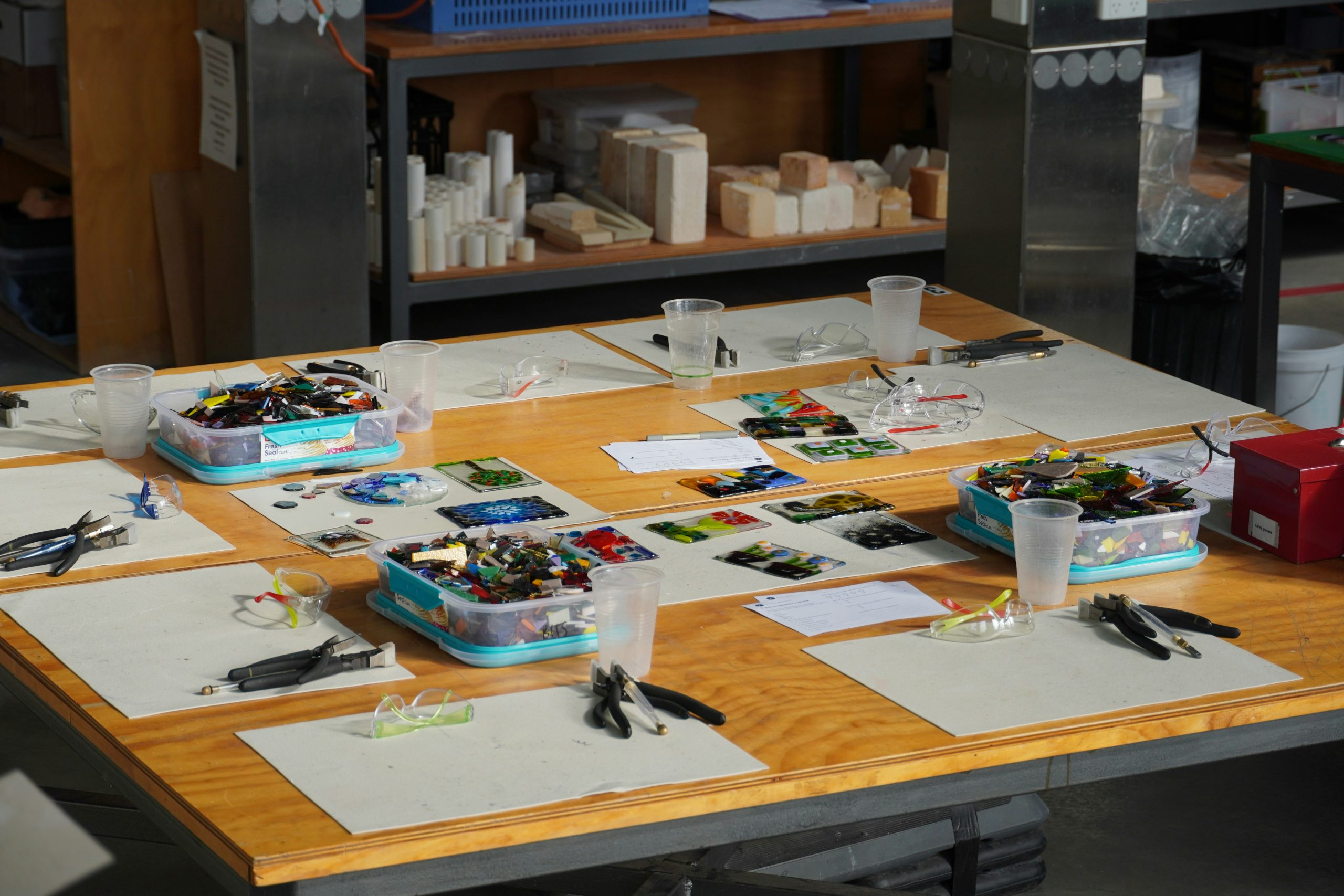 An art workshop with mosaic tiles against a crafting table background, with various art supplies on the table.