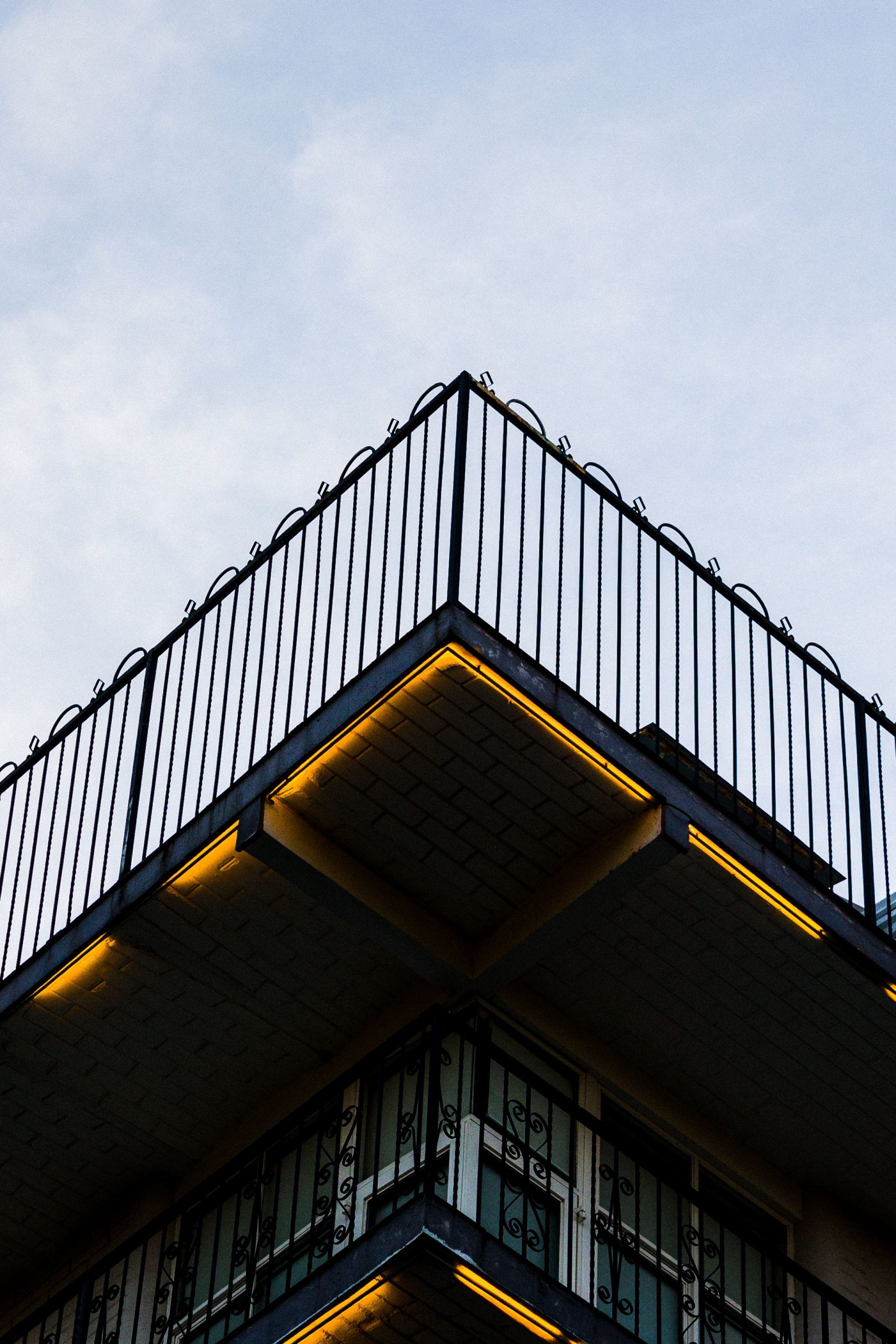 An upward view of a balcony with railing and illuminated underlighting against a clear sky