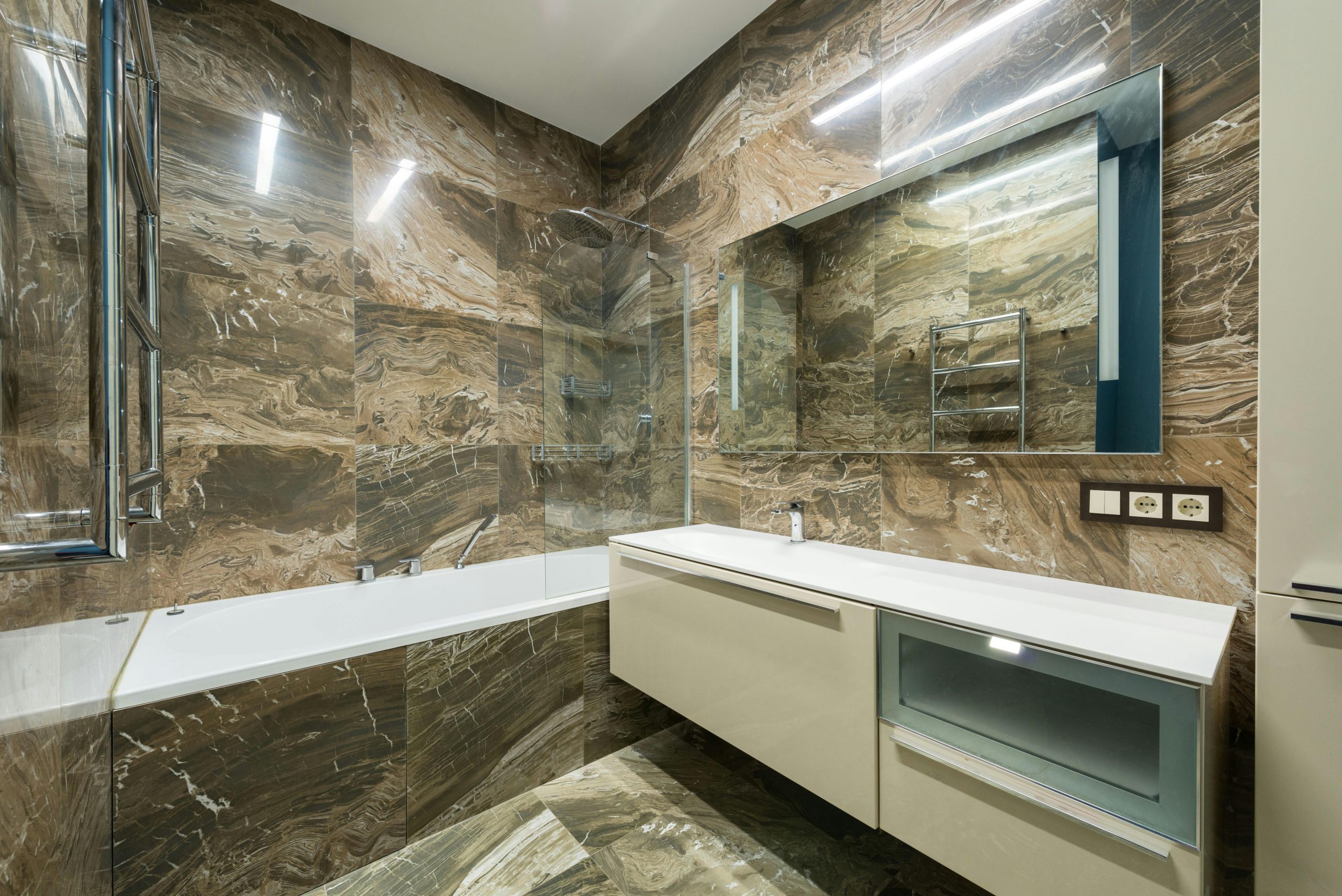 Bathtub placed near wall sink on cabinet at wall with mirror placed in contemporary bathroom with marble tiles at home