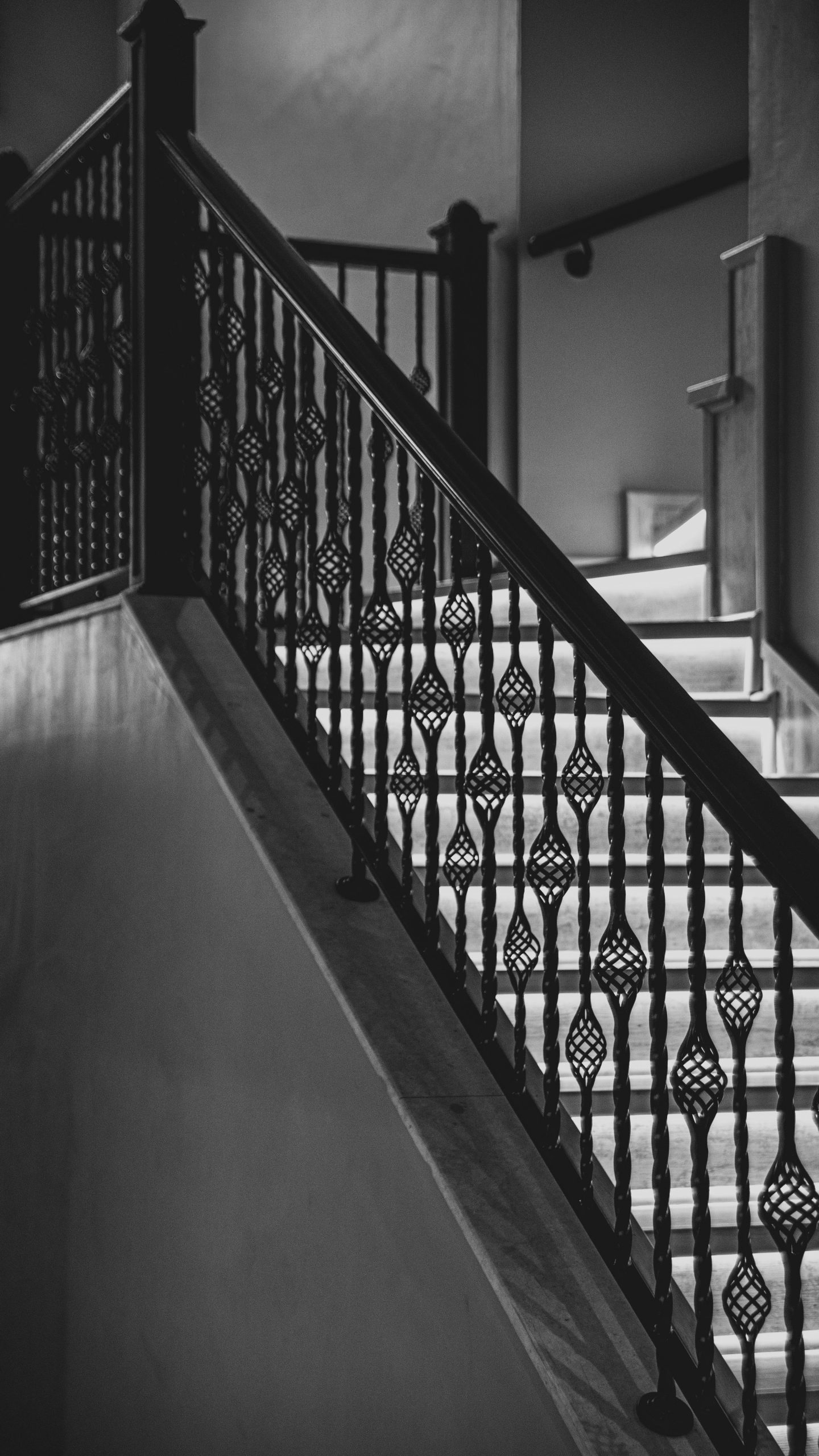 Black and white photo of a staircase with ornate iron railings in an indoor setting.