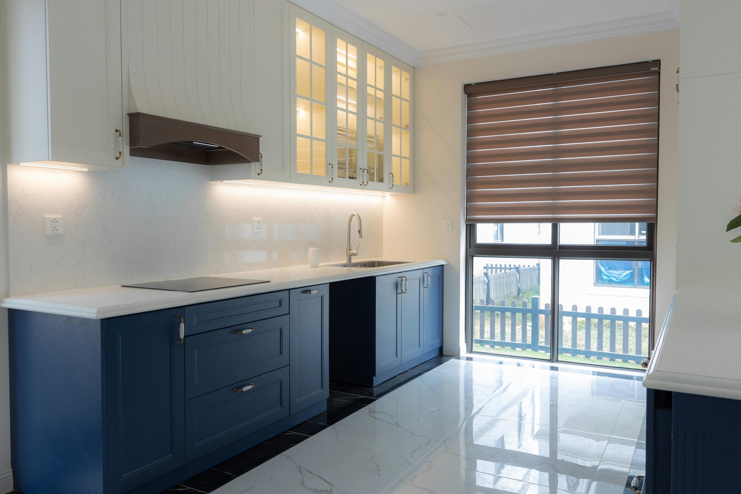 Bright modern kitchen featuring blue cabinetry, marble countertops, and ample natural light through large windows.