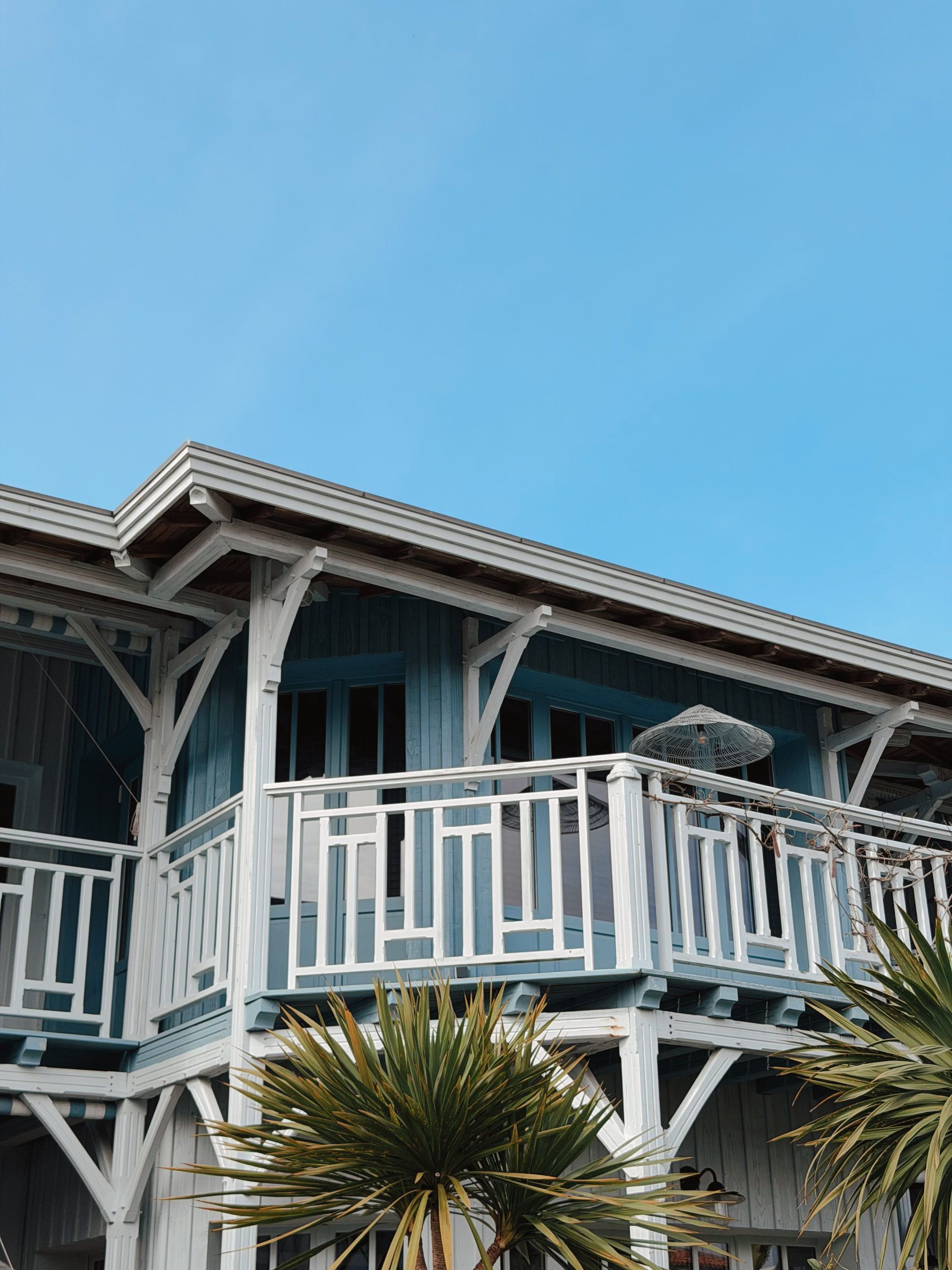 Charming white wooden beach house with balcony under a bright blue sky.