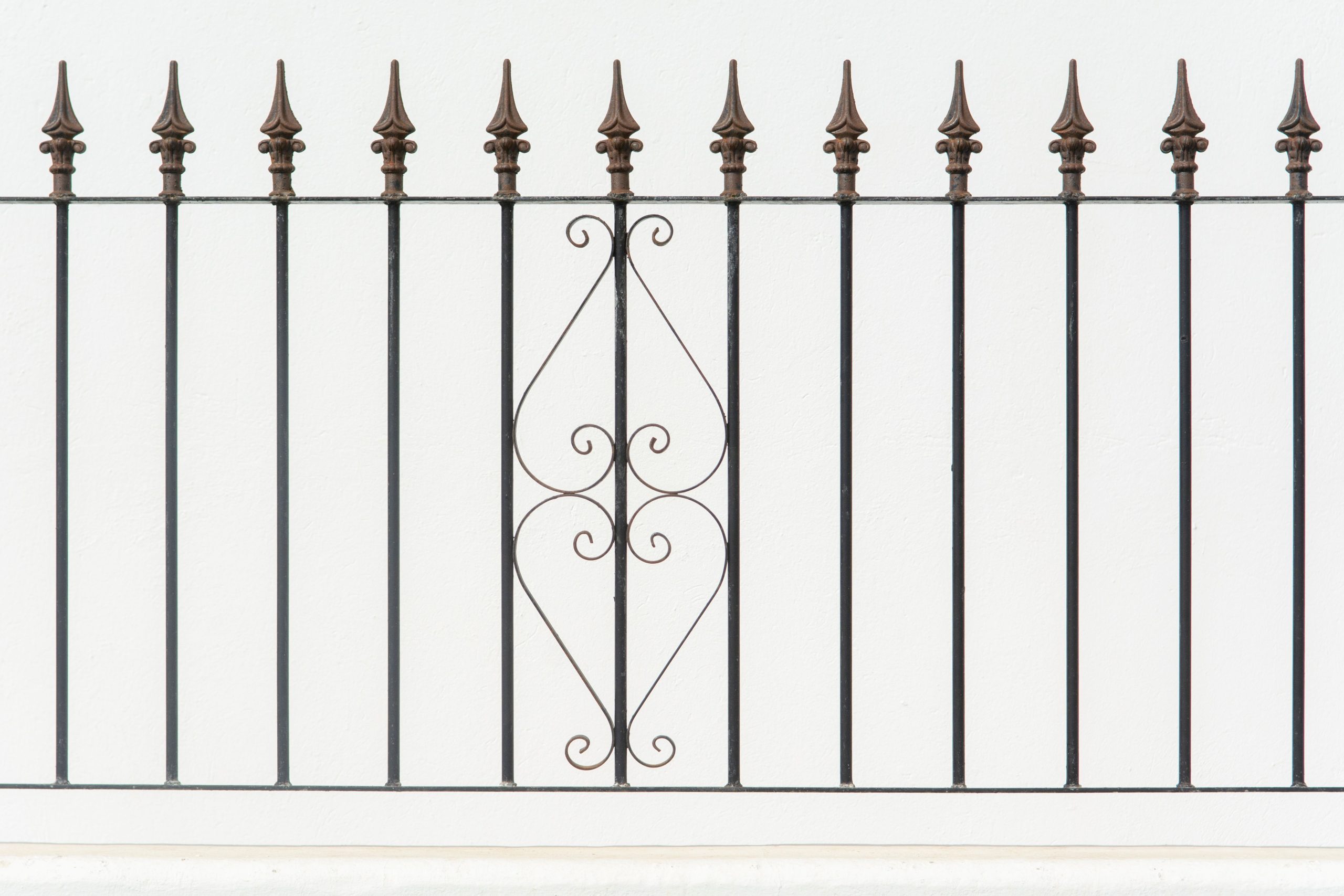 Close-up of an ornate wrought iron fence with symmetrical decorative patterns and pointed finials.