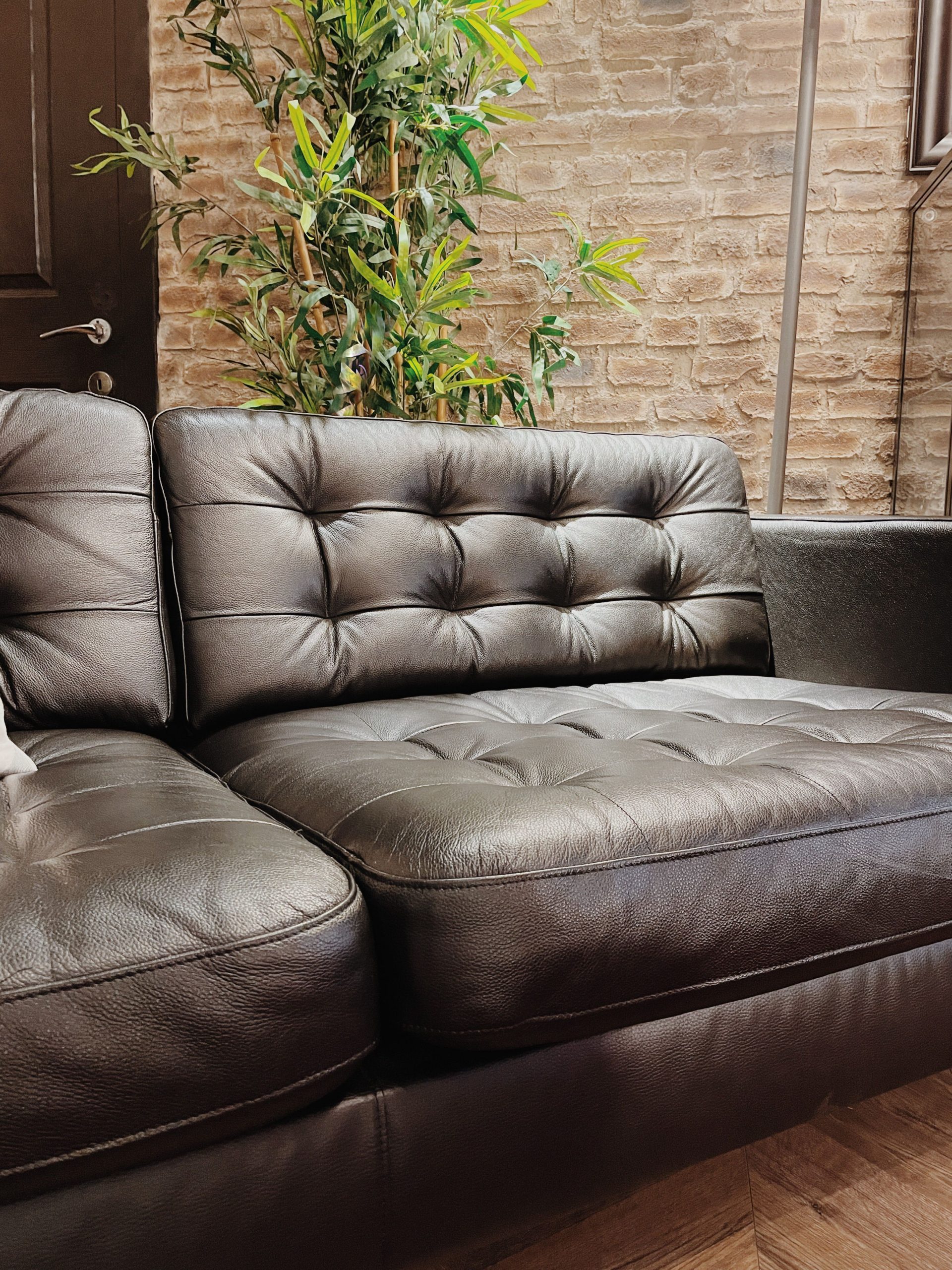 Close-up of black leather sofa against a brick wall with green plants, in a modern indoor setting.