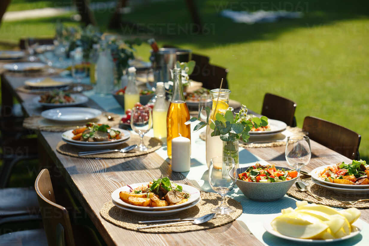 Close up shot of a set table at a summer garden party. Table setting with glasses, lemonade, fresh fruits and salad and the delicate floral decoration. stock photo