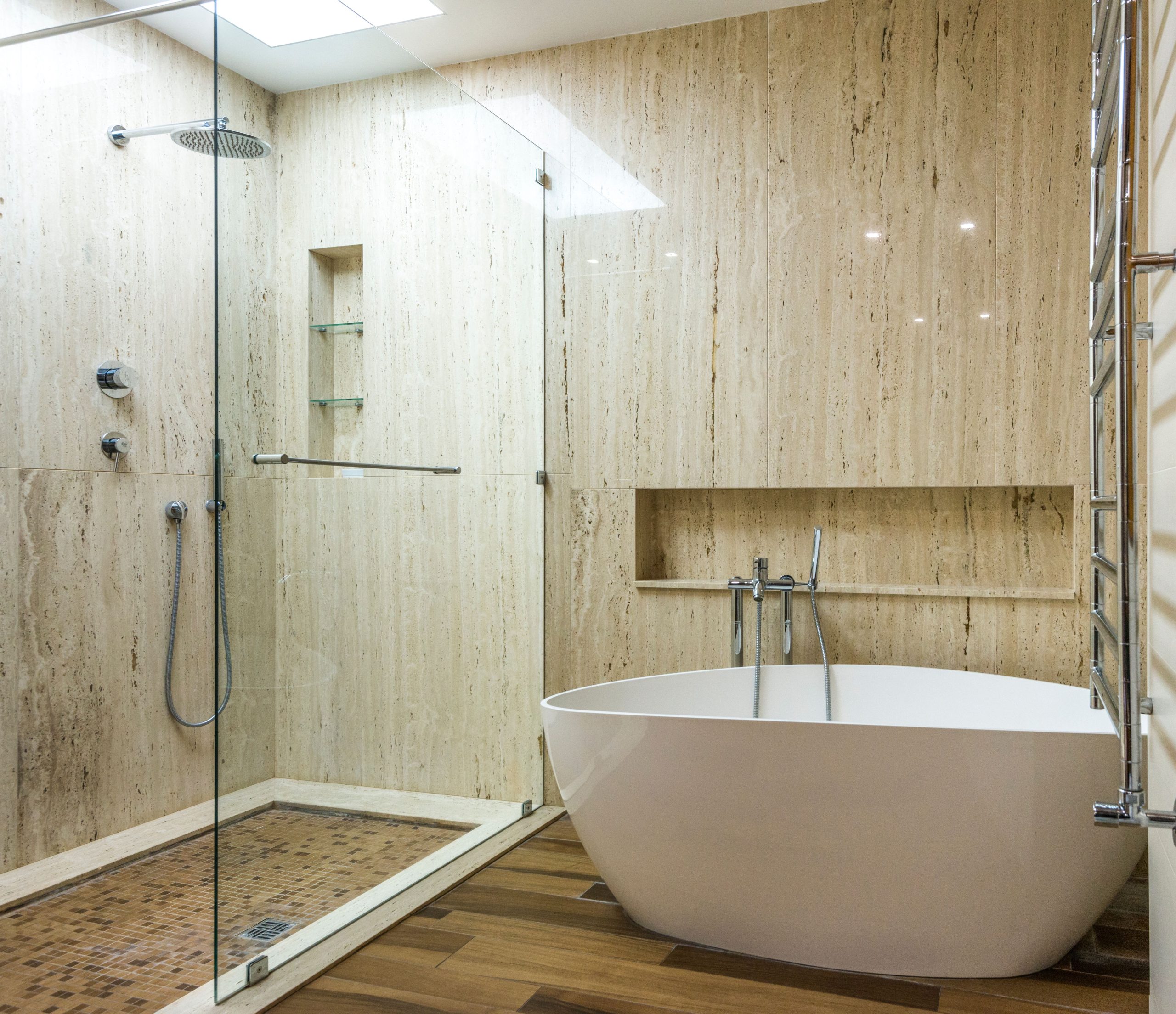 Contemporary bathroom featuring a marble wall, glass shower, and stylish bathtub.