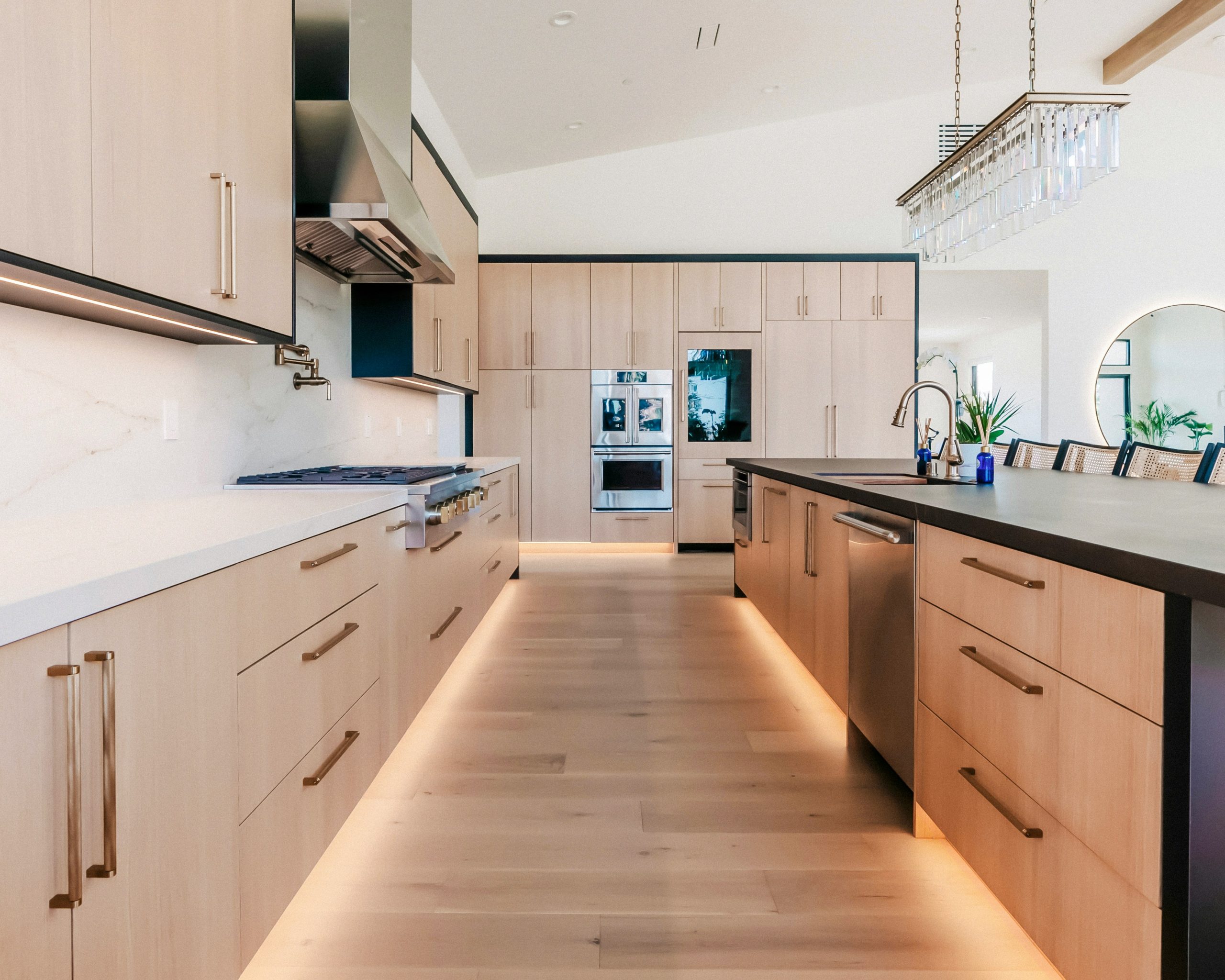 Contemporary kitchen featuring flat panel wood cabinets, oversized black framed windows, white countertops, and a spacious island. A bright, luxury kitchen design blending natural materials with clean
