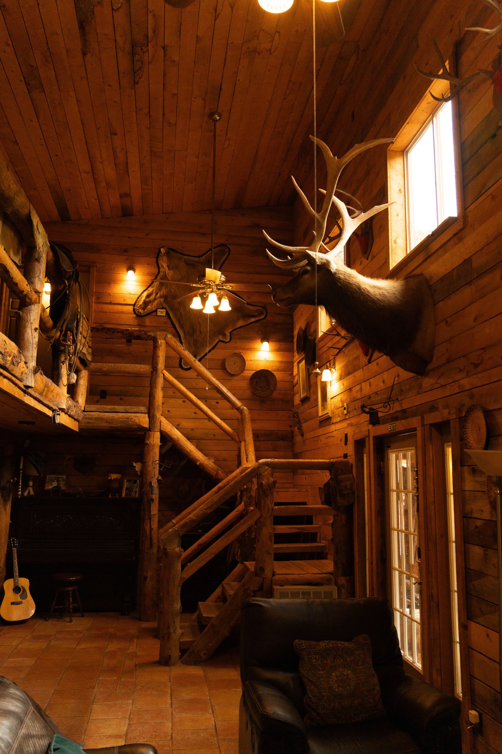 Cozy wooden cabin interior with rustic decor, mounted deer head, and warm lighting.