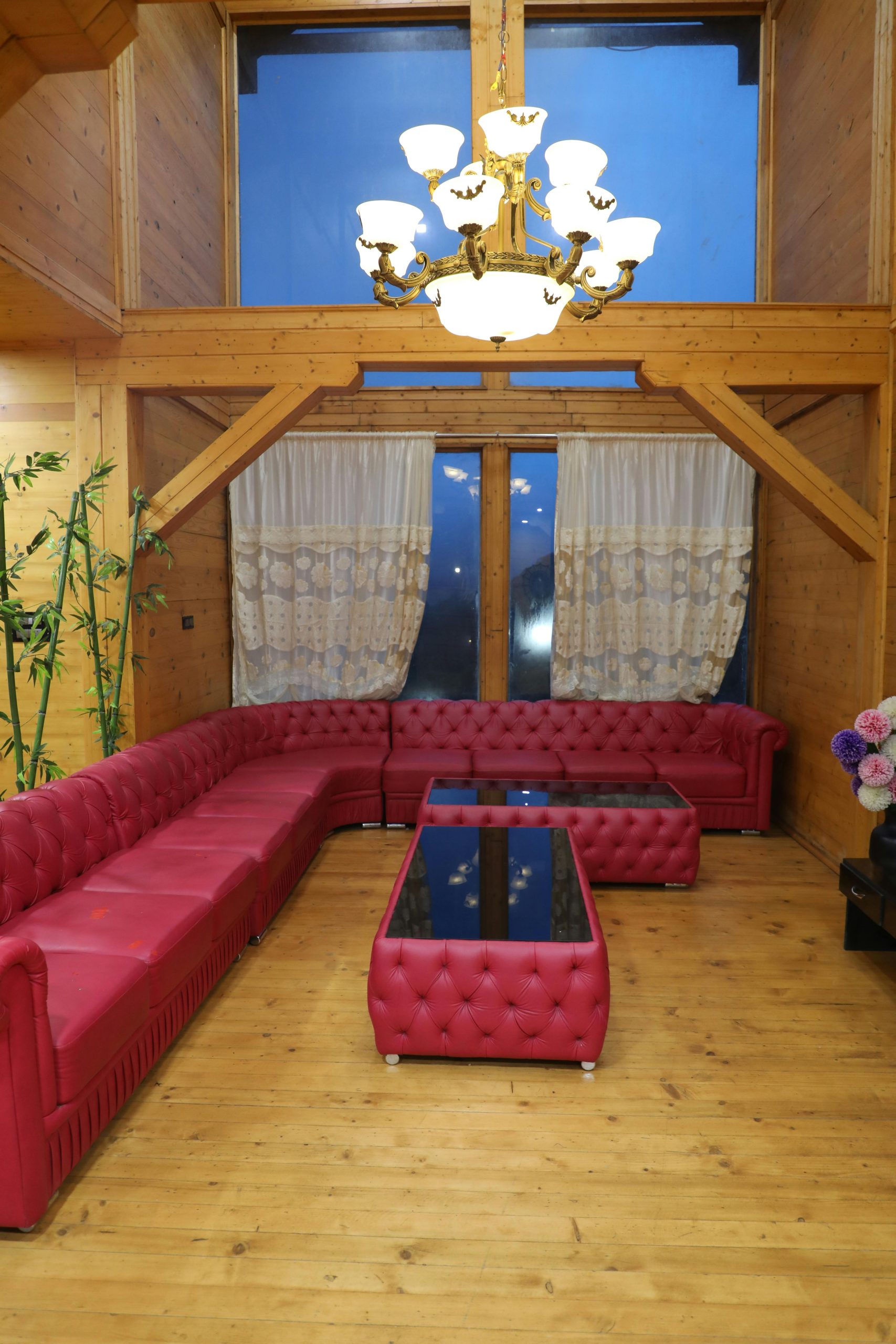 Cozy wooden living room featuring red sofas, glass tables, and a chandelier.