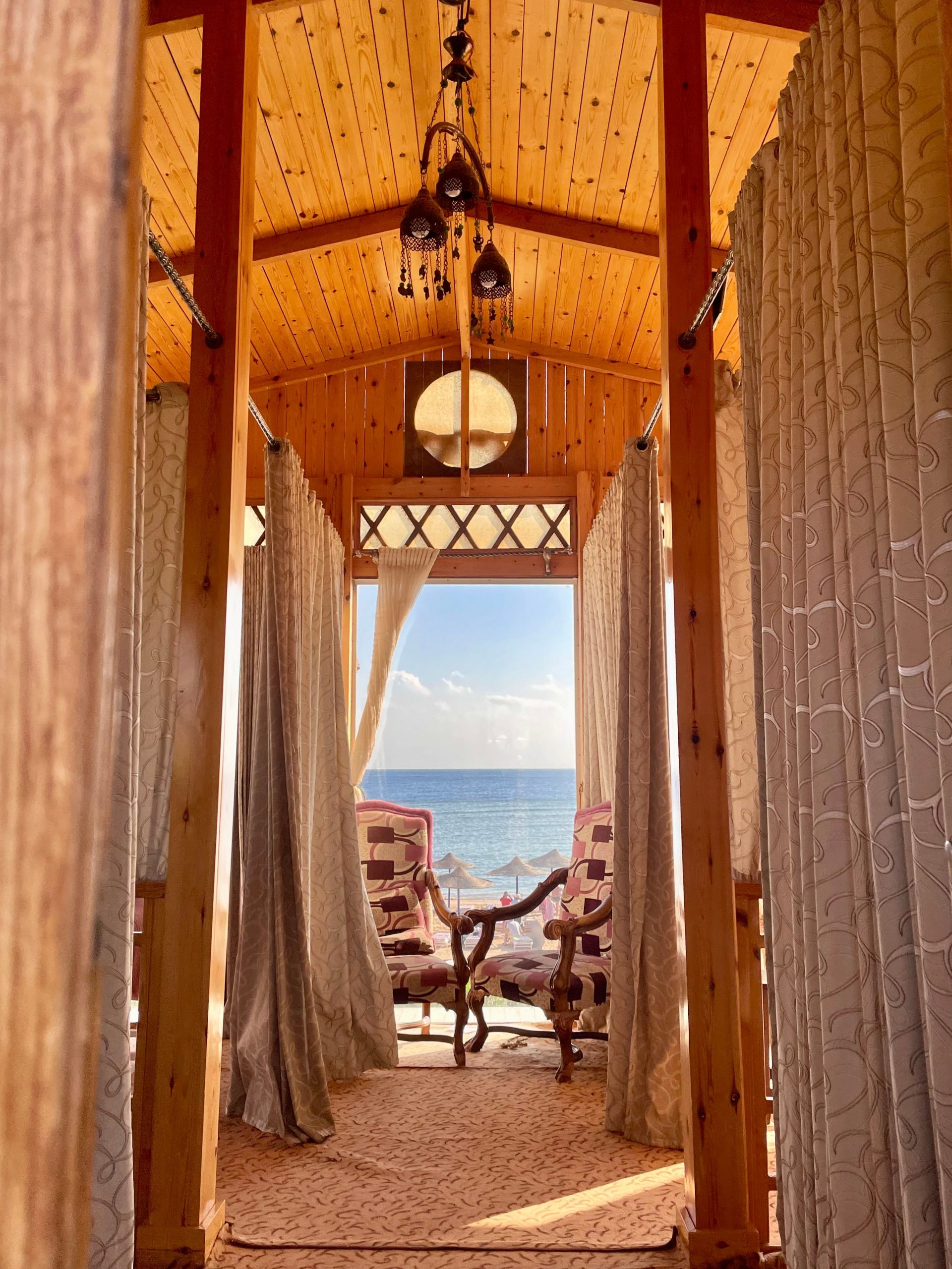 Elegant beachfront cabana featuring armchairs and curtains with ocean view, ideal for a seaside retreat.