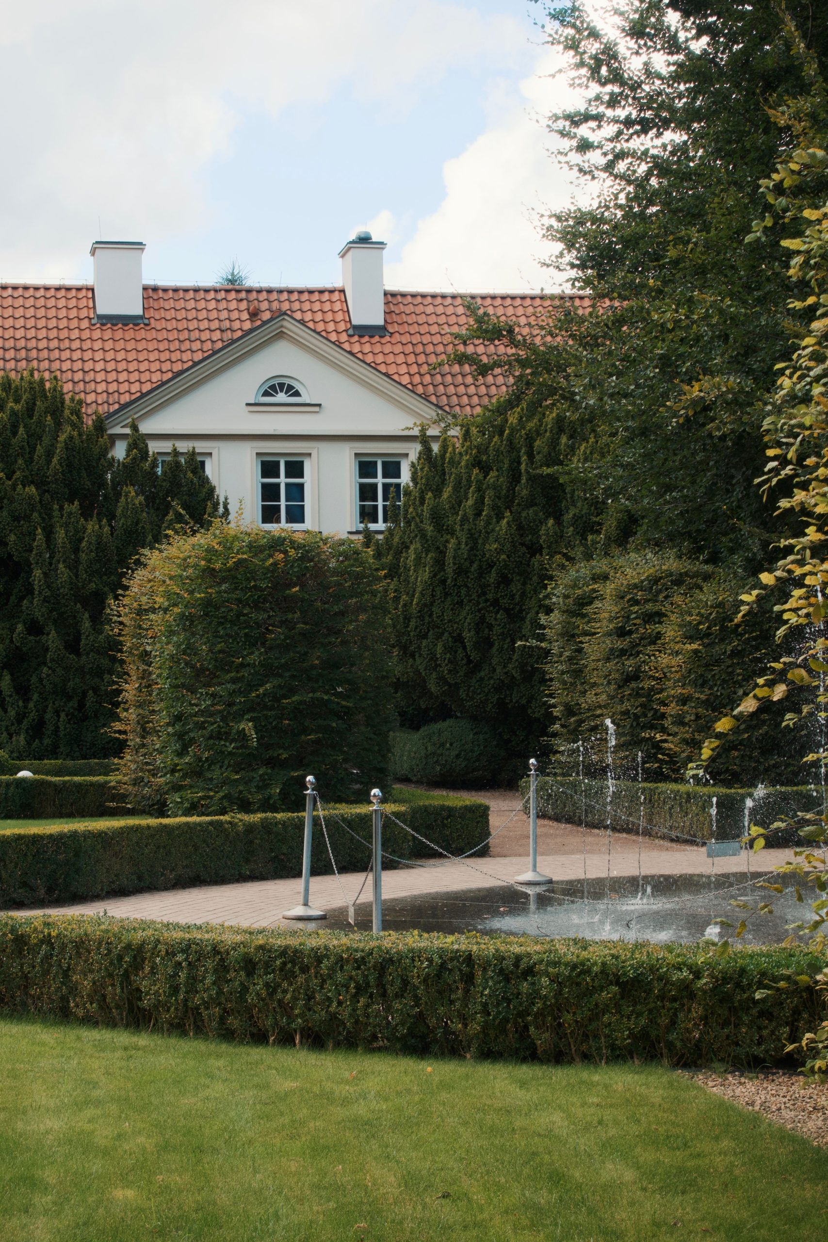 Elegant European house with a well-maintained garden and fountain, exuding classic charm.