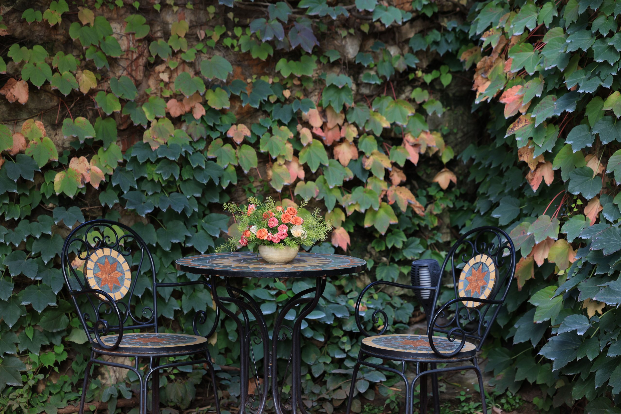 Elegant garden setting with a mosaic table and chairs, surrounded by lush ivy.