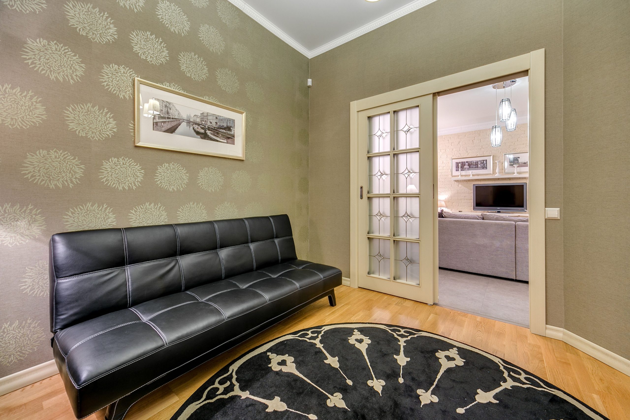 Elegant living room interior with black leather sofa and patterned wallpaper.