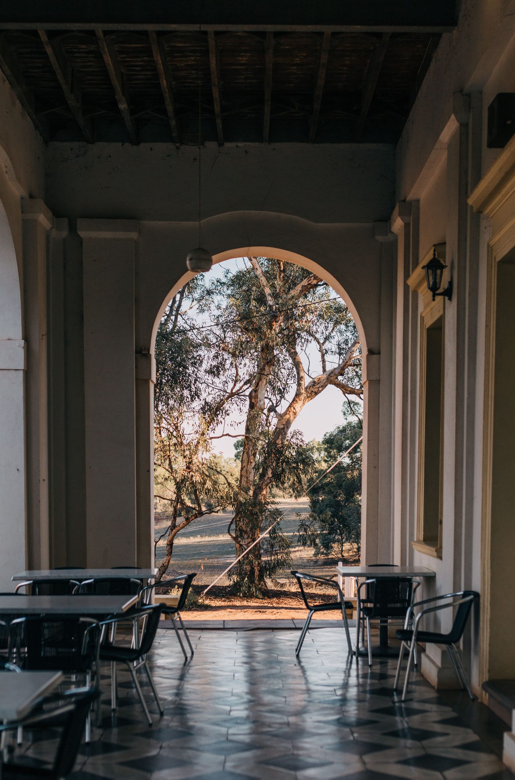 Elegant outdoor patio with tables and chairs under an archway on sunny day.