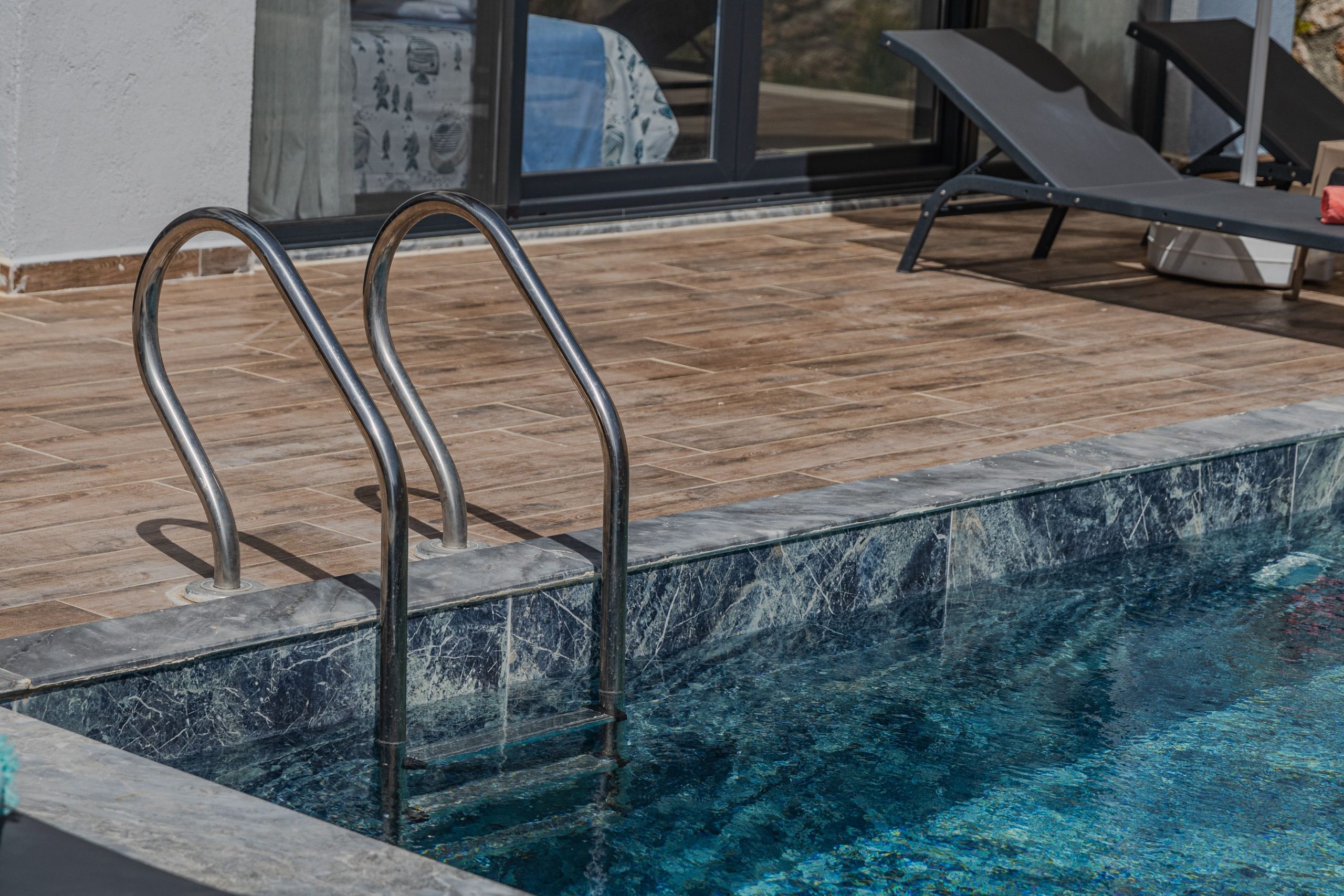 Elegant pool area with marble edging, wooden deck, and modern loungers, perfect for relaxation.