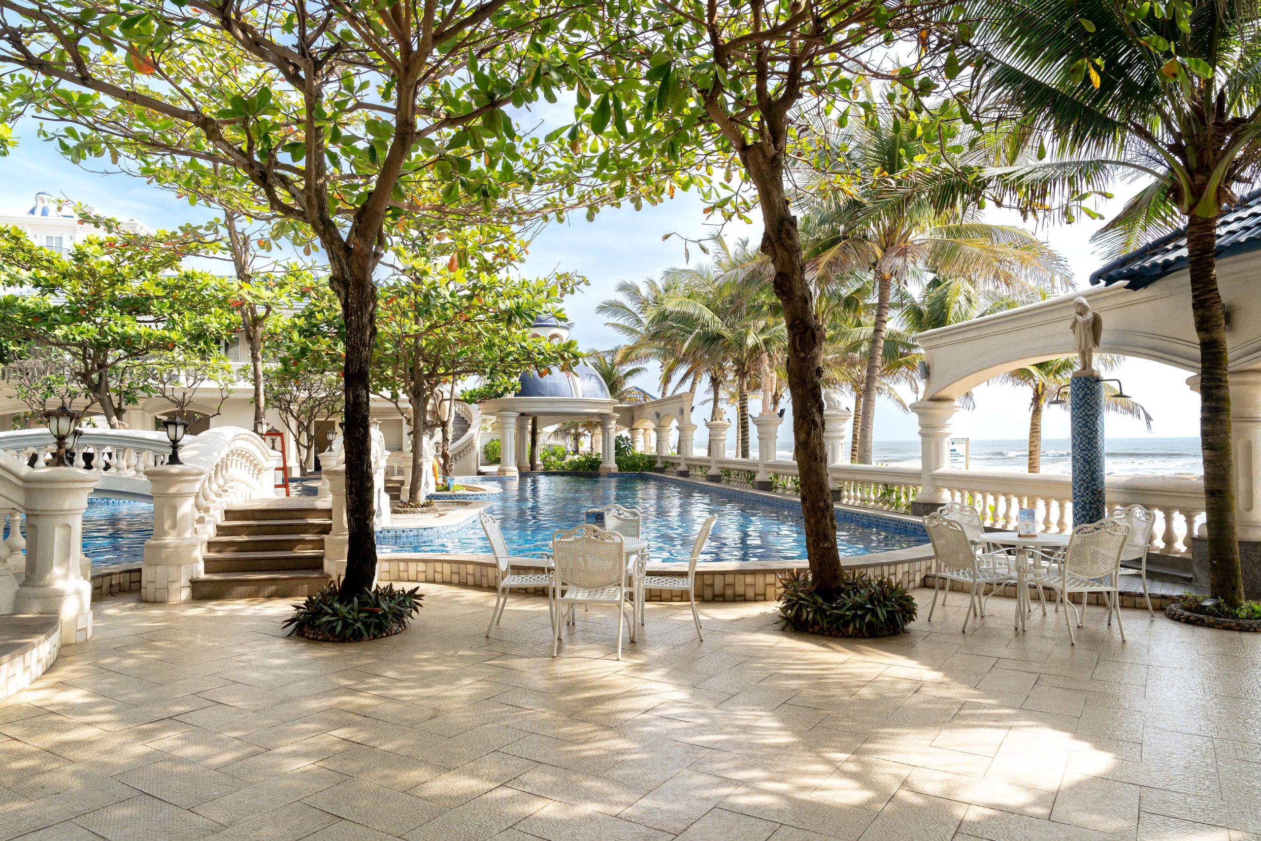Elegant poolside patio with tropical palm trees and ocean view, perfect for relaxation.