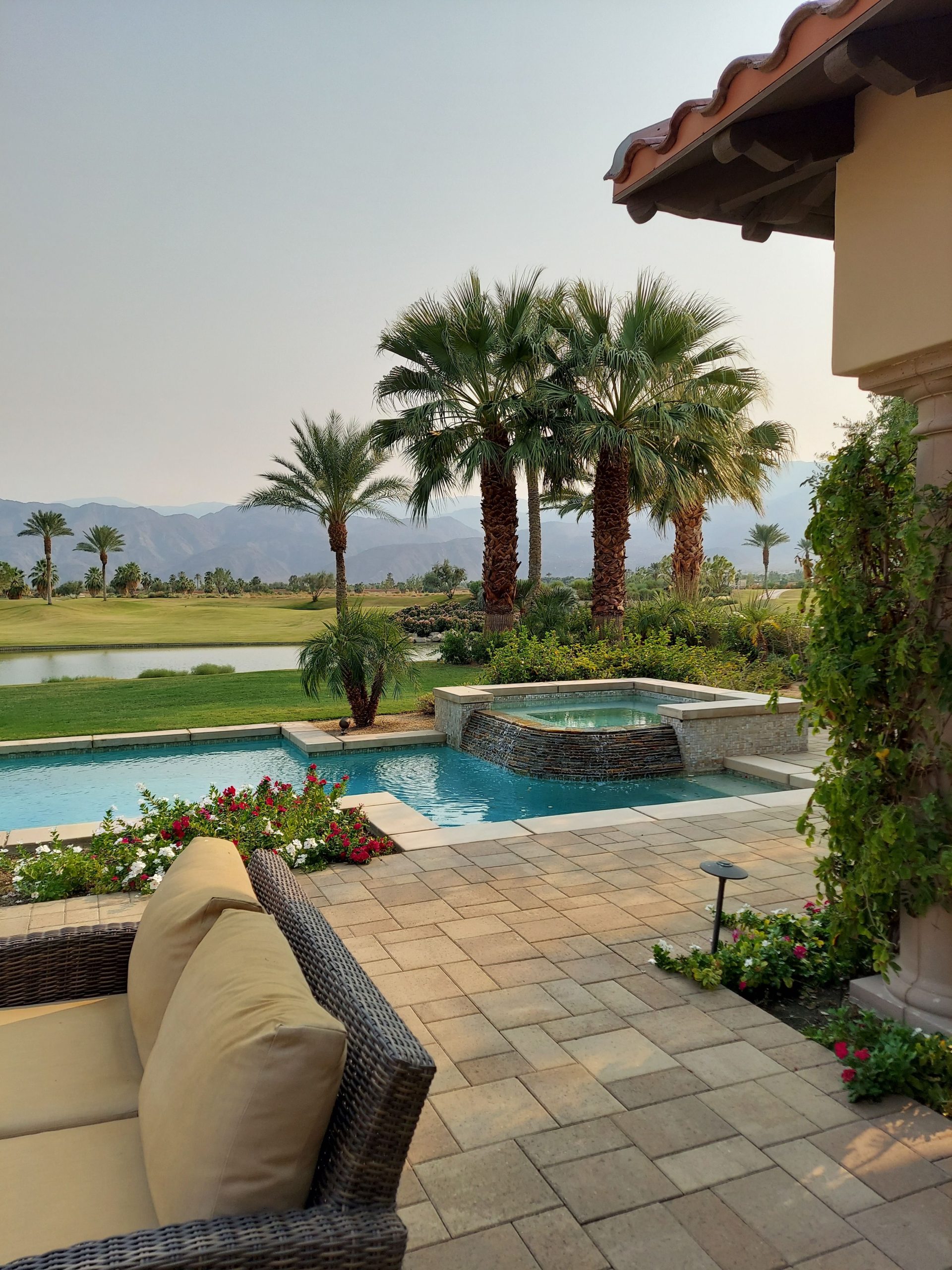 Elegant tropical patio with pool, palm trees, and mountain view under clear skies.