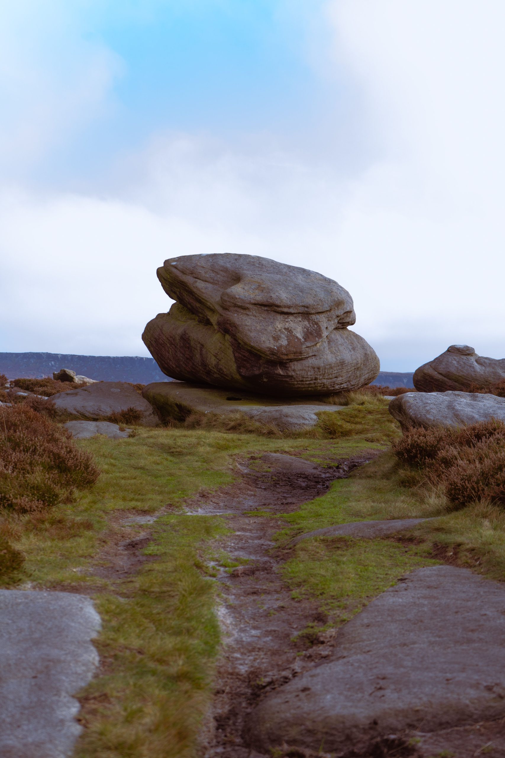 Explore a breathtaking path with a majestic boulder atop a cliff, surrounded by nature's beauty.
