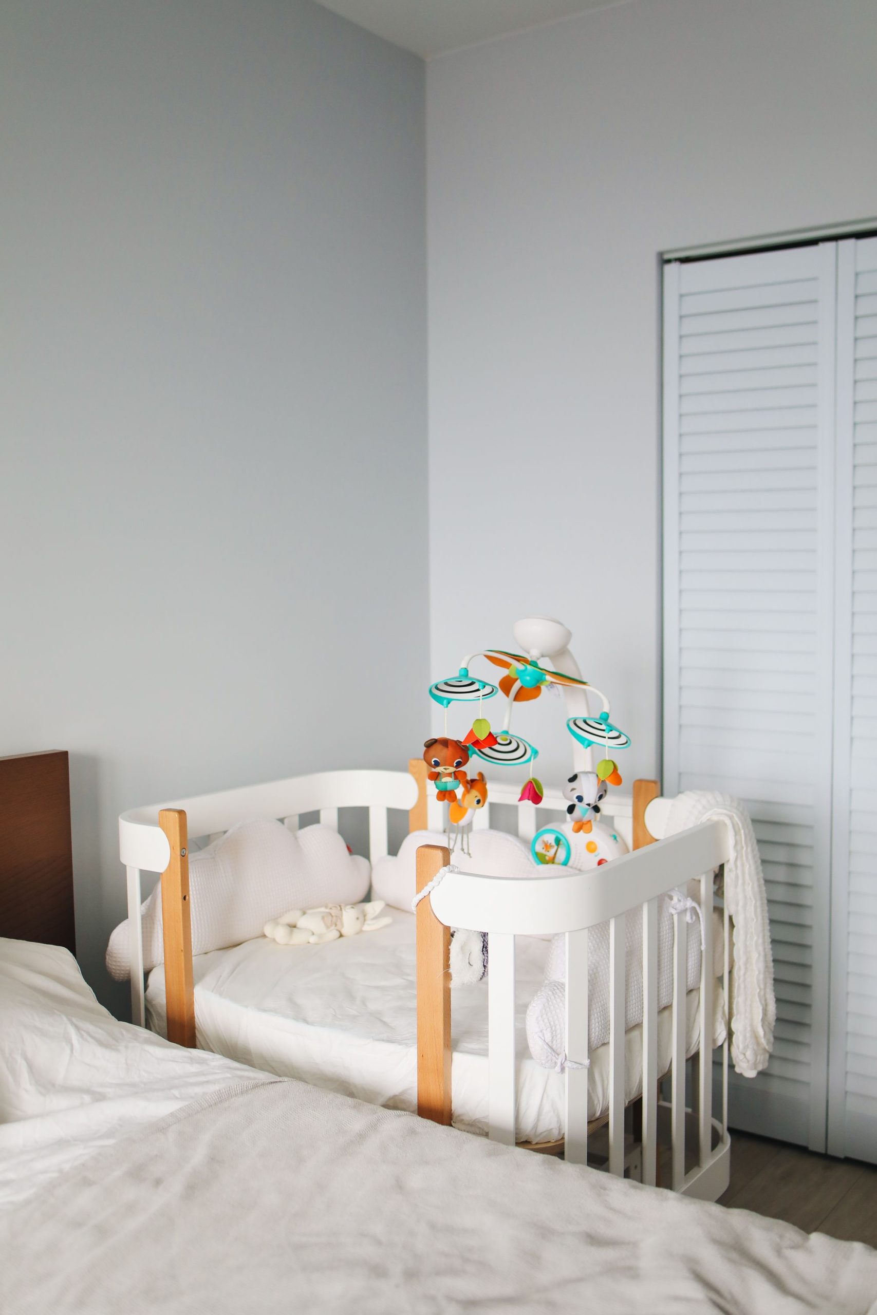 Interior of cozy light bedroom with white cute wooden crib locating in corner between bed and built in wardrobe during morning