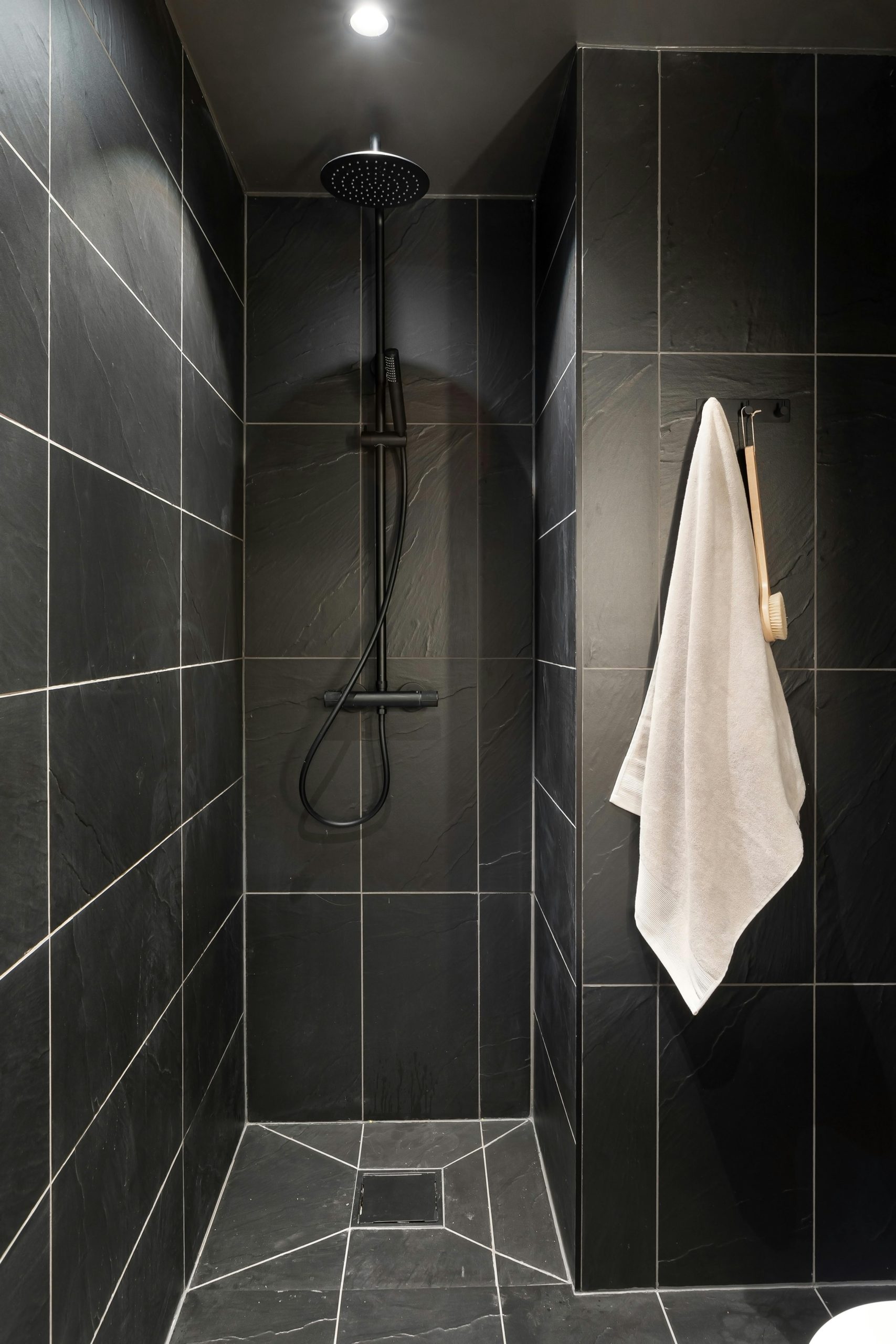 Minimalist black tiled shower with hanging white towel and modern fixtures.