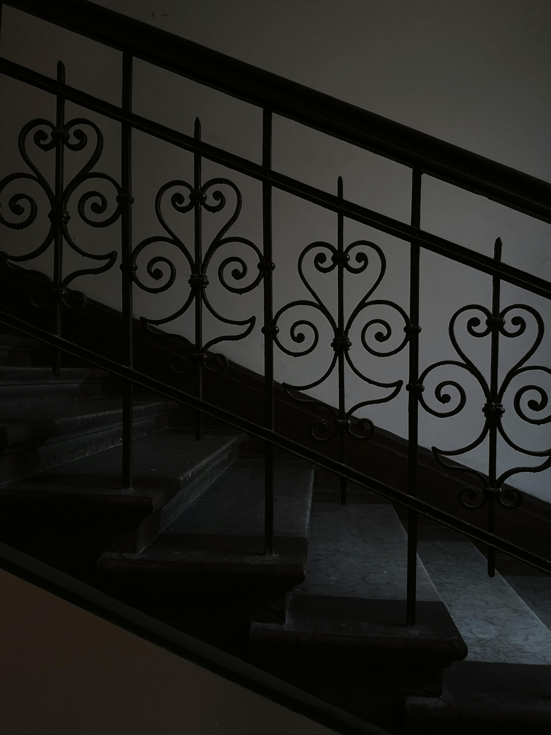 Ornate iron railing with intricate design on a dimly lit staircase indoors.