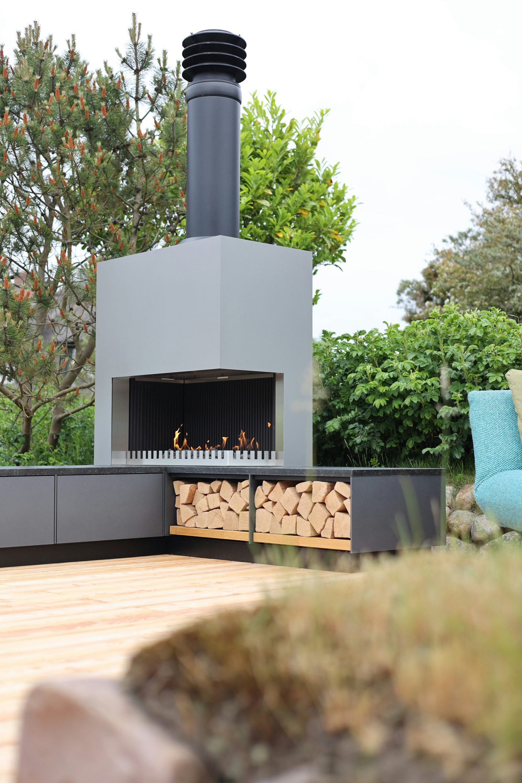 Outdoor fireplace with burning logs and firewood on a deck.