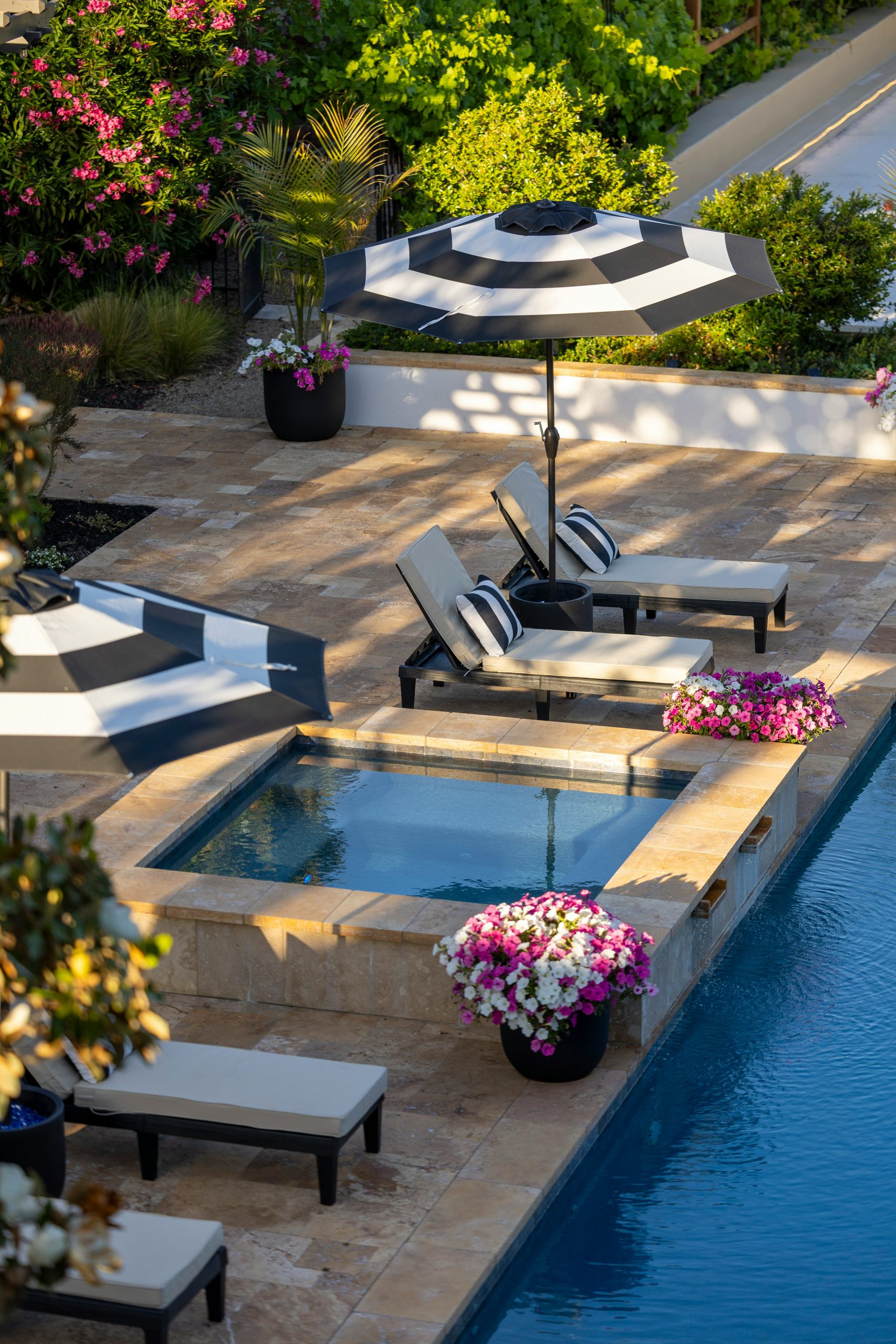 Poolside area with hot tub, lounge chairs, umbrella, and flowers.