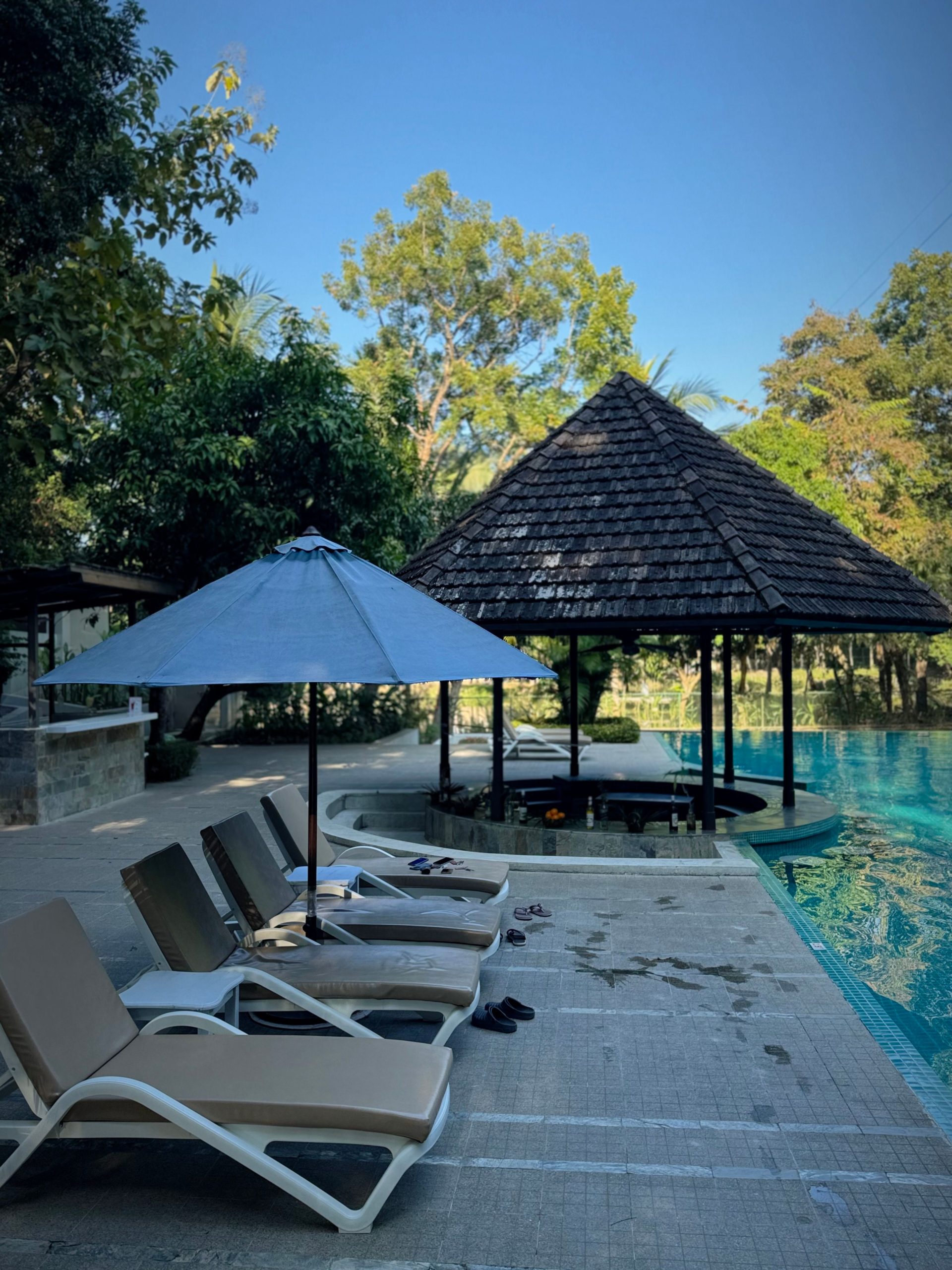 Relaxing poolside scene with loungers, umbrella, and gazebo under a clear blue sky.