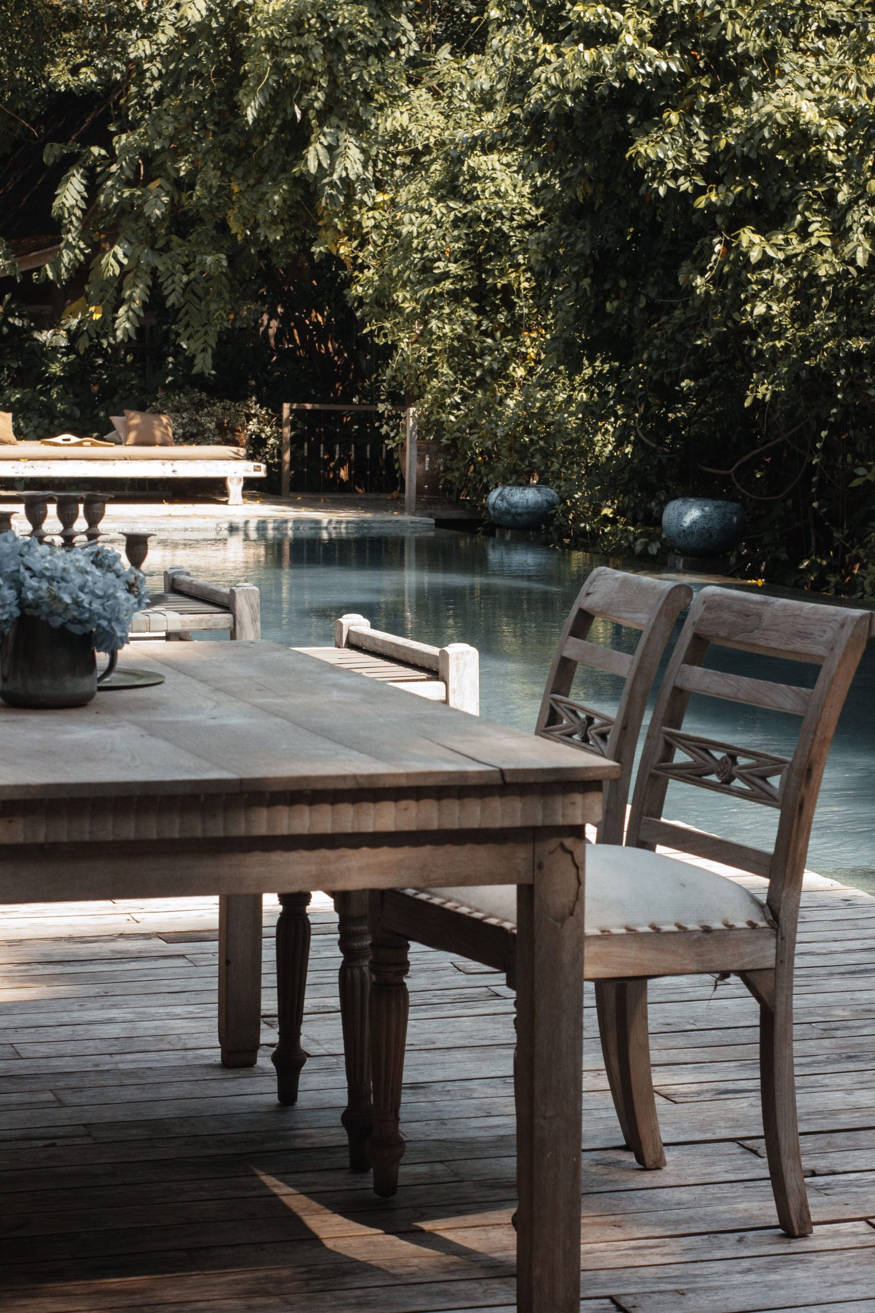 Rustic wooden table and chairs on a serene outdoor deck by the pool, surrounded by lush greenery.